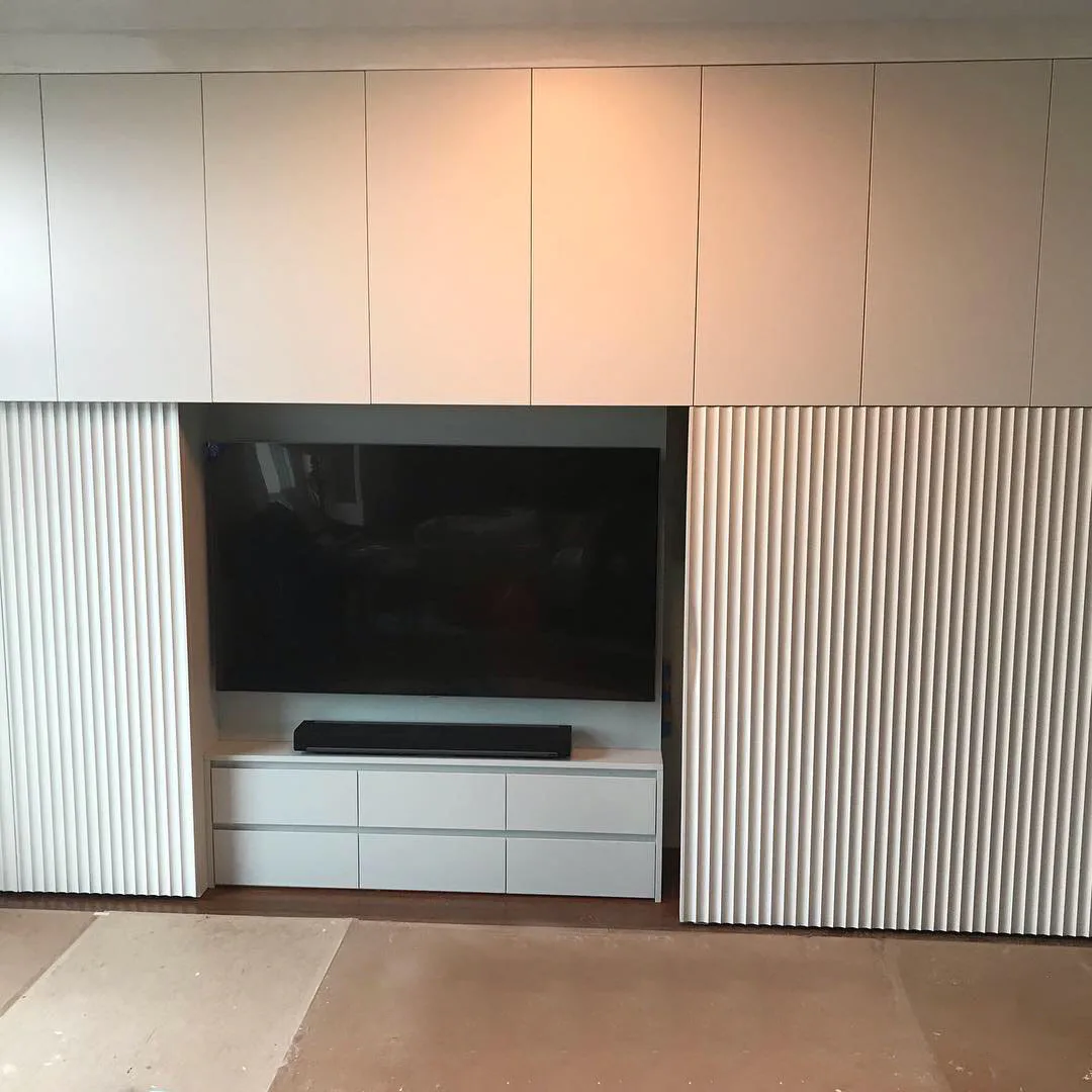 Modern white media wall with integrated TV niche, soundbar, storage drawers, and vertical ribbed side panels in a minimalist interior by Tercio.
