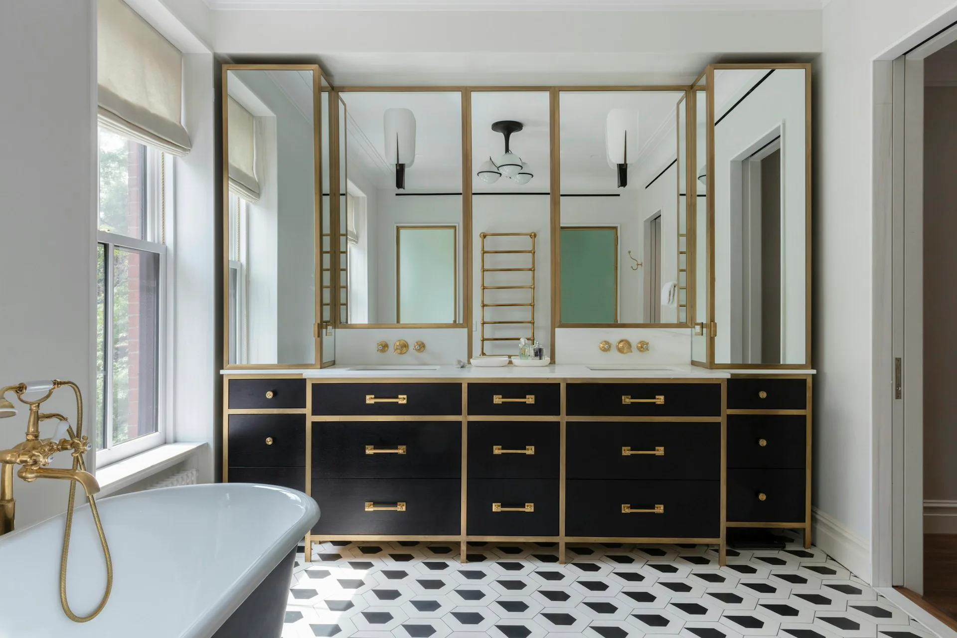 Luxurious bathroom with black vanity, brass fixtures, mirrored wall, and geometric black-and-white tile flooring by The Brooklyn Studio.