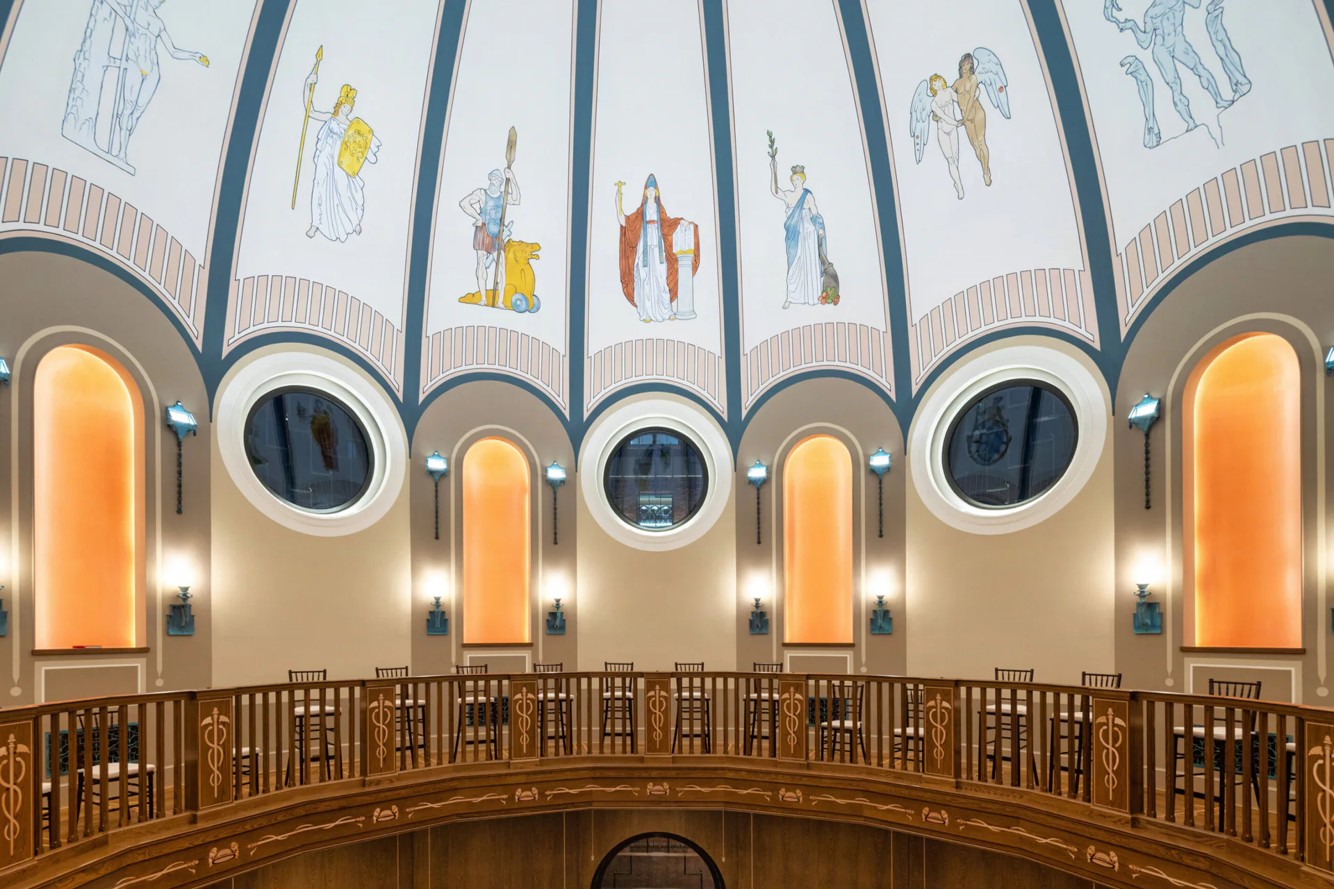 Drum-shaped interior with cream walls, ornate wooden railing, circular windows with warm backlighting, and decorative ceiling murals by The Lighting Practice.