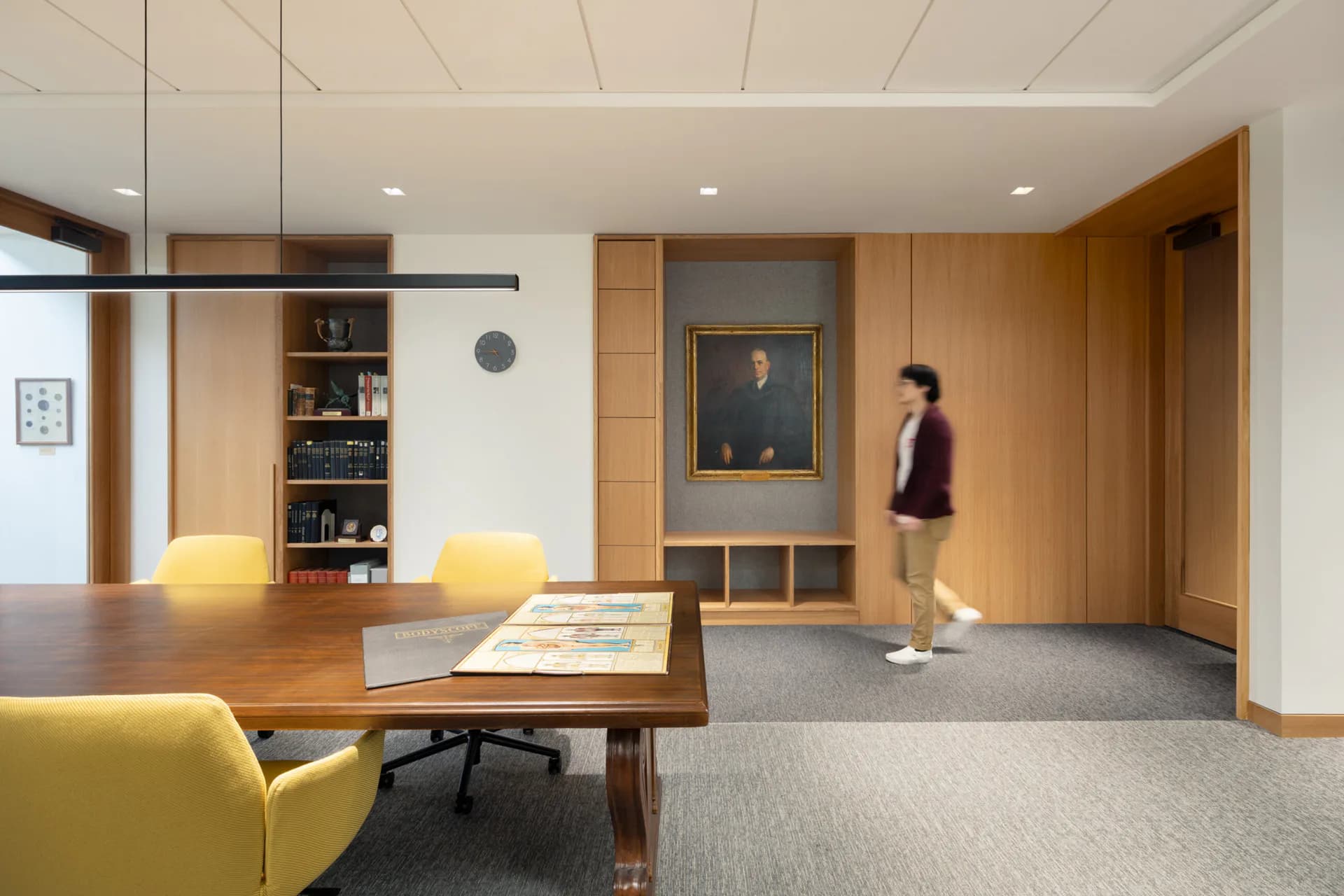 Modern office lounge with warm wood paneling, yellow seating, and ambient ceiling lighting by The Lighting Practice.