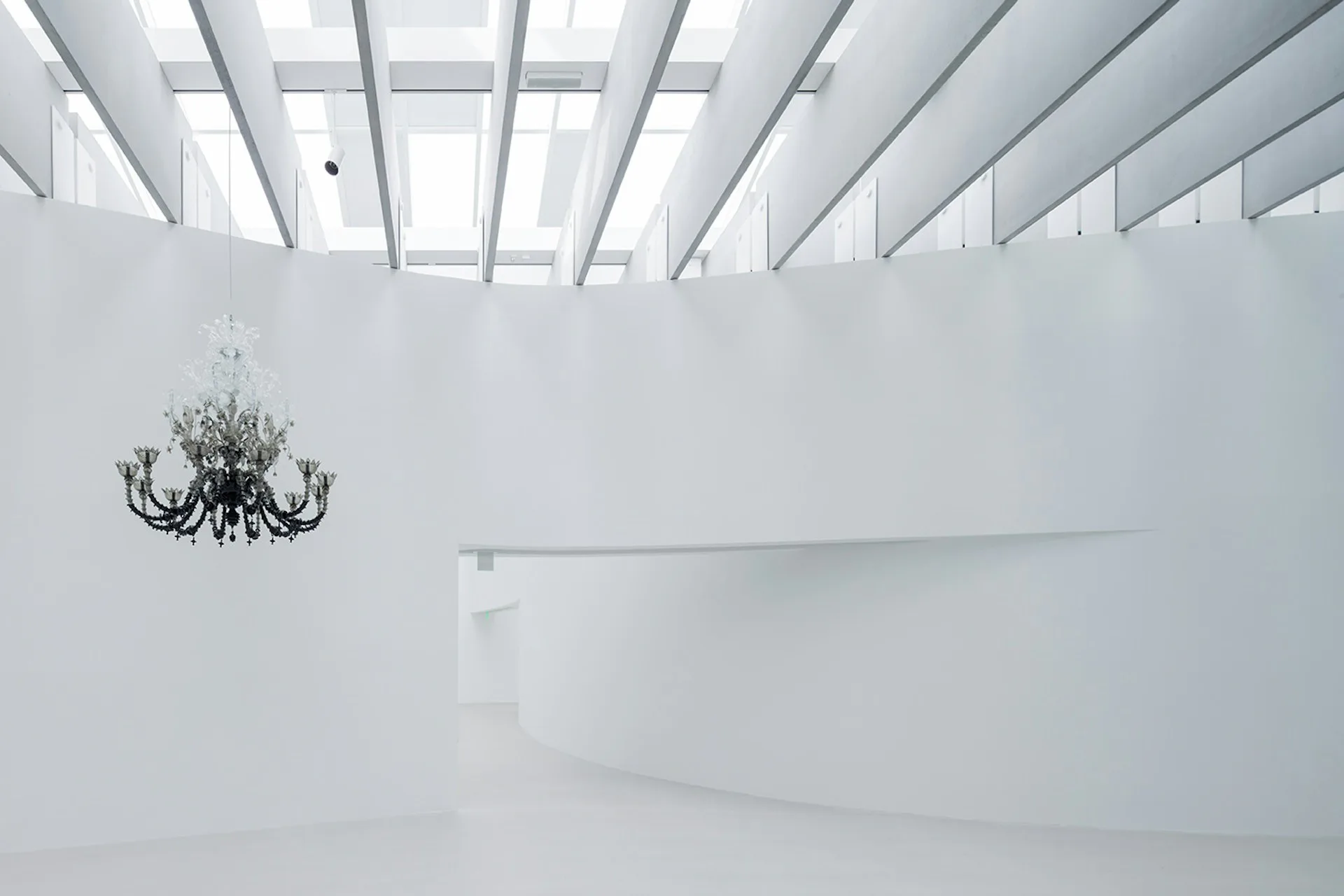 Minimalist white interior with skylight ceiling and black chandelier, featuring clean geometric forms and ethereal lighting characteristic of Thomas Phifer and Partners.
