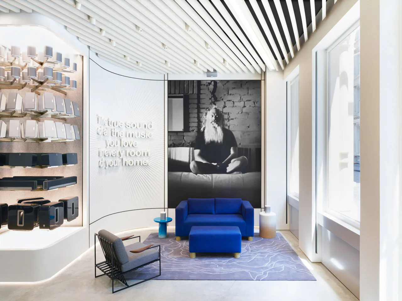 Modern retail showroom with striped ceiling, blue modular sofa, gray accent chair, and black-and-white photography wall installation by Tietz-Baccon.