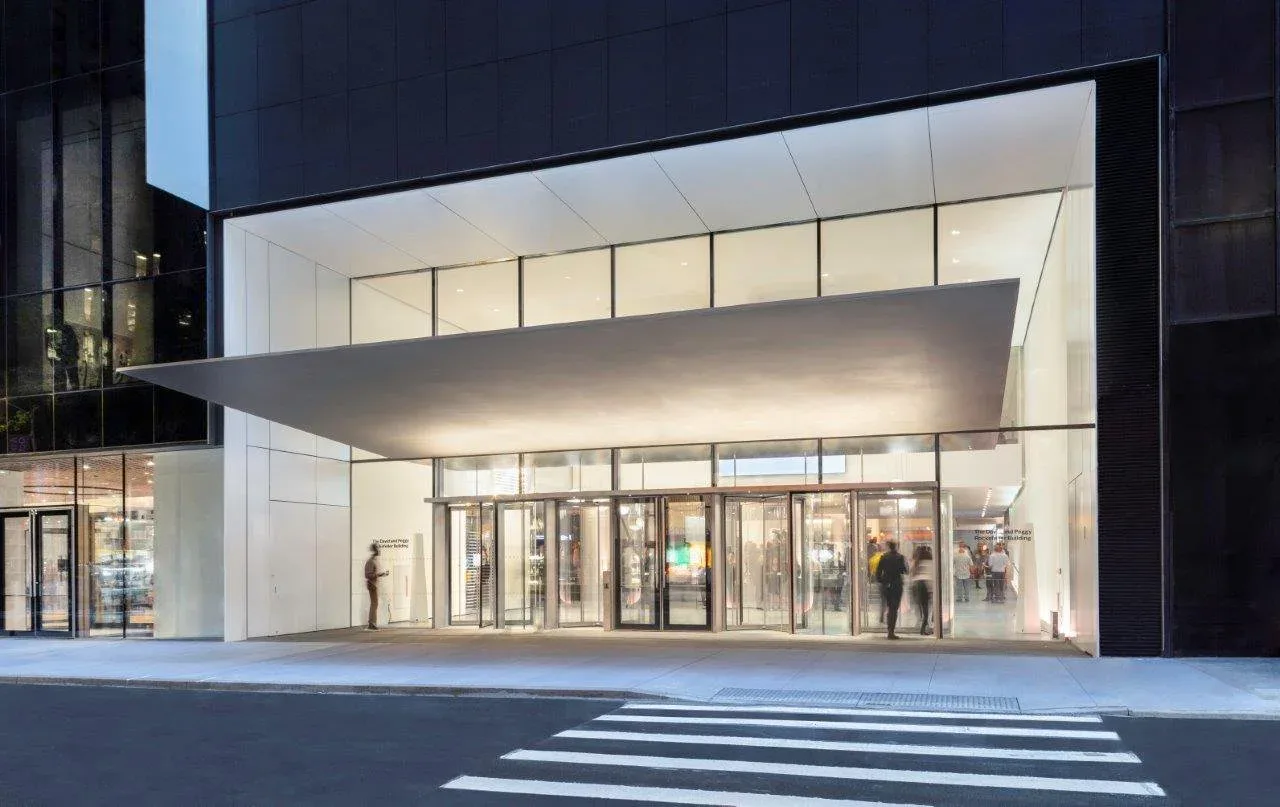 Modern storefront with minimalist white facade, horizontal window bands, and dramatic cantilevered awning, photographed at dusk by Tillotson Design Associates.