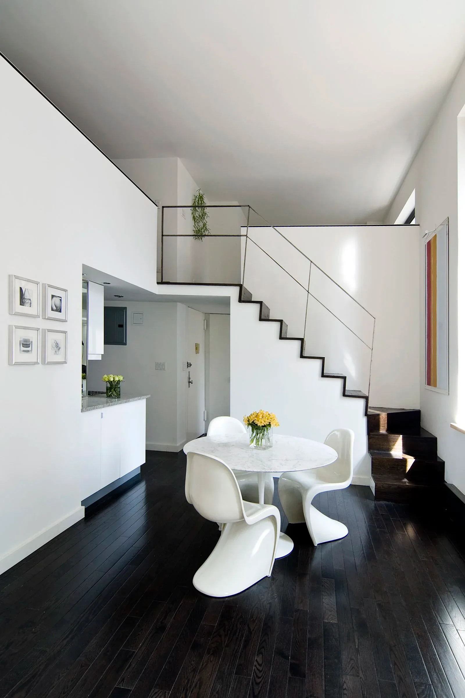 Minimalist loft interior with white walls, black flooring, sculptural staircase, and round white dining table by Tinmouth Chang Architects.