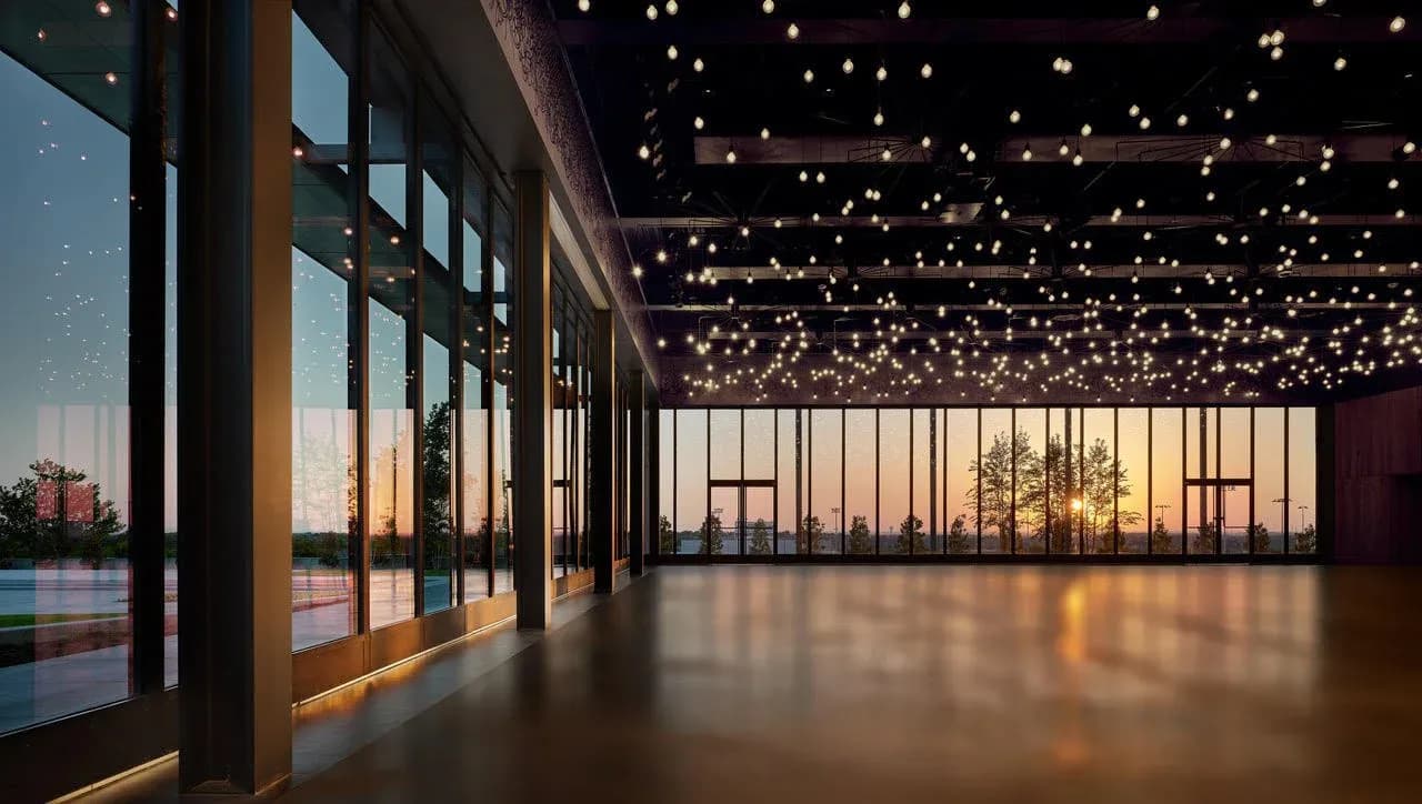 A modern event space with floor-to-ceiling windows overlooking a sunset, polished concrete floors, and an expansive starlit ceiling installation by Tirschwell & Co.