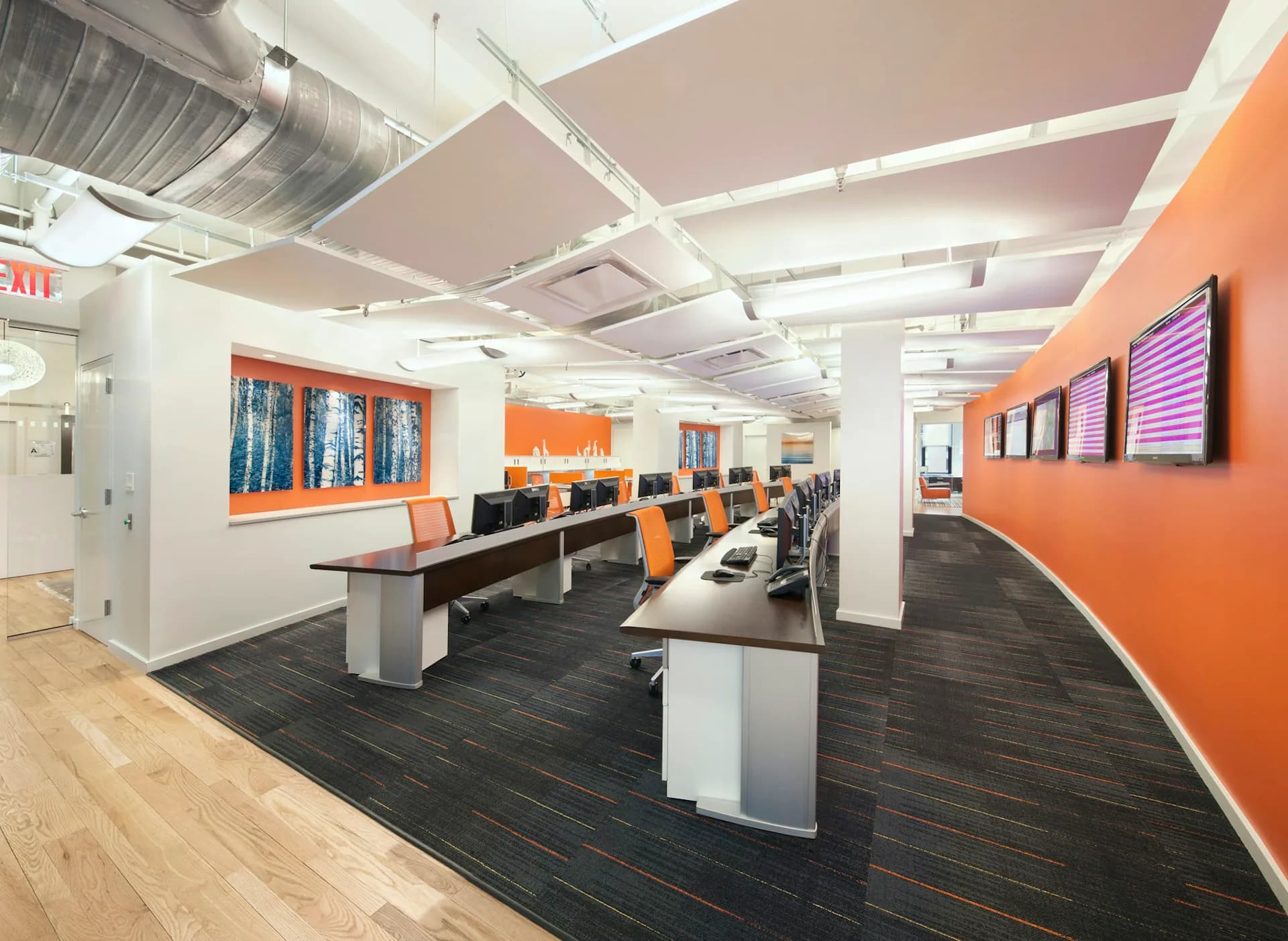 Modern open-plan office with orange accent walls, dark wood flooring, white ceiling beams, and integrated workstations by TPD Architecture.