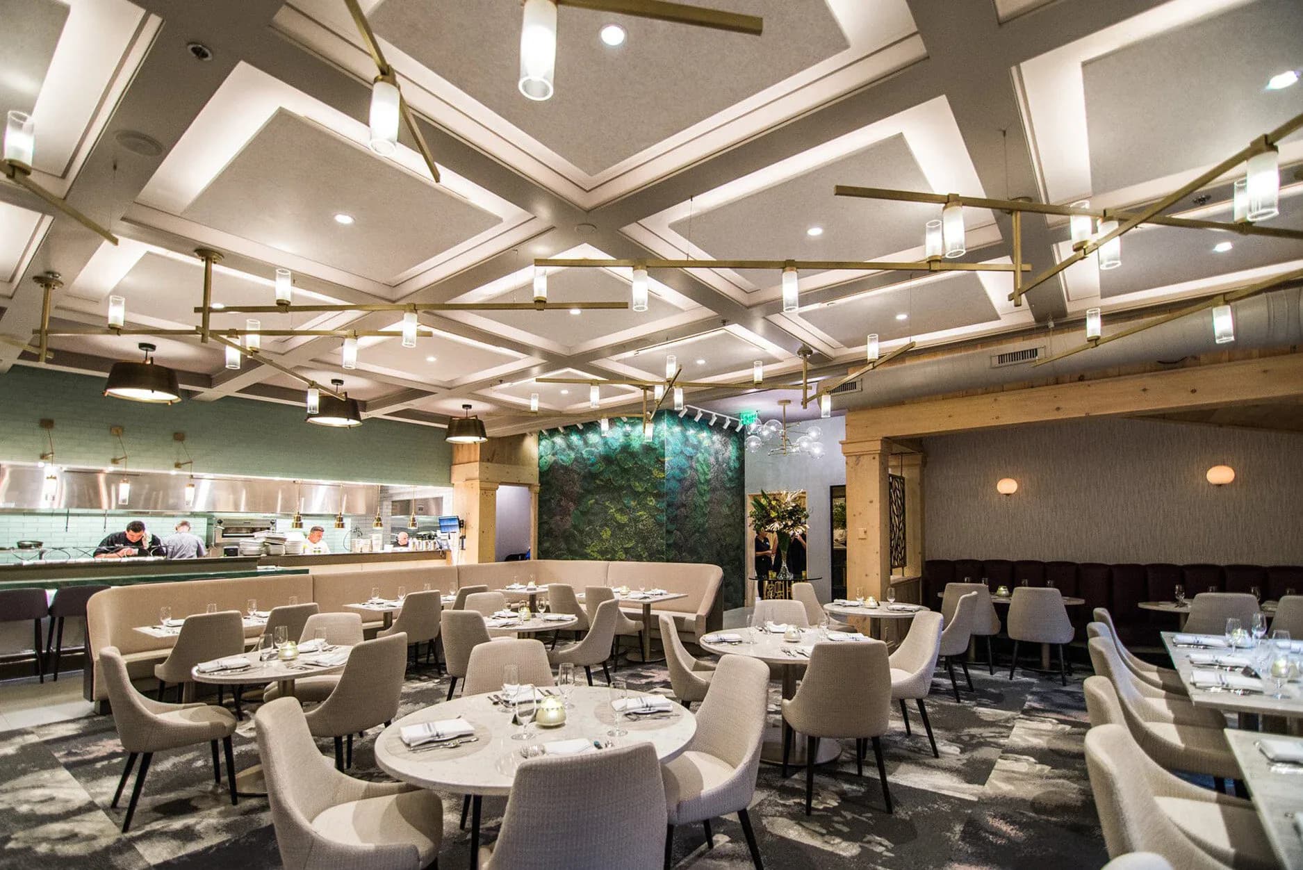 Fine dining restaurant with sculptural coffered ceiling, cream upholstered chairs, round tables, and open kitchen view, designed by TPD Architecture.