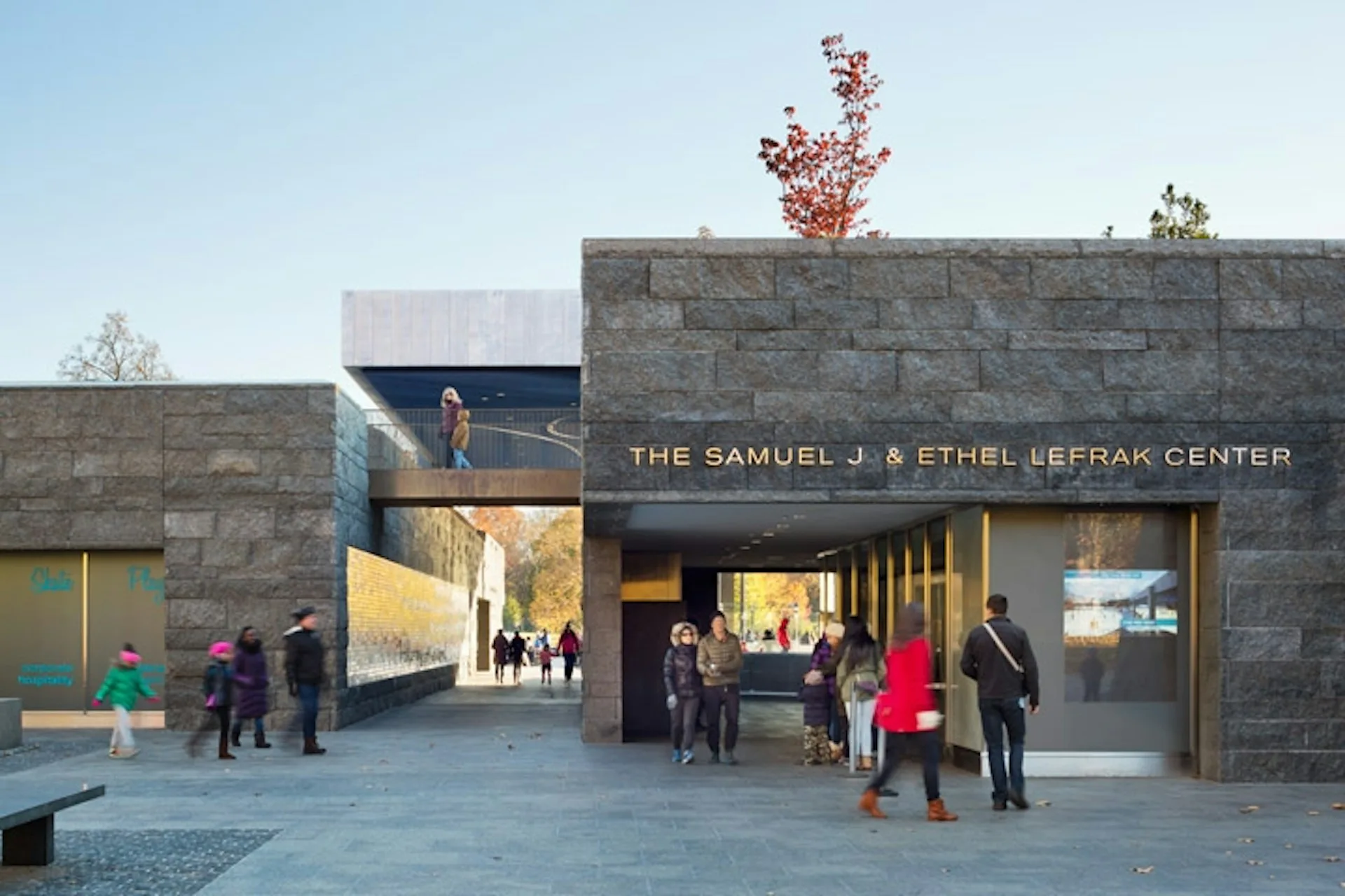 The Samuel J. & Ethel LeBrak Center features a stone facade with large glazed openings and a modern entrance pavilion, with visitors gathered in the plaza by Tod Williams Billie Tsien Architects | Partners.