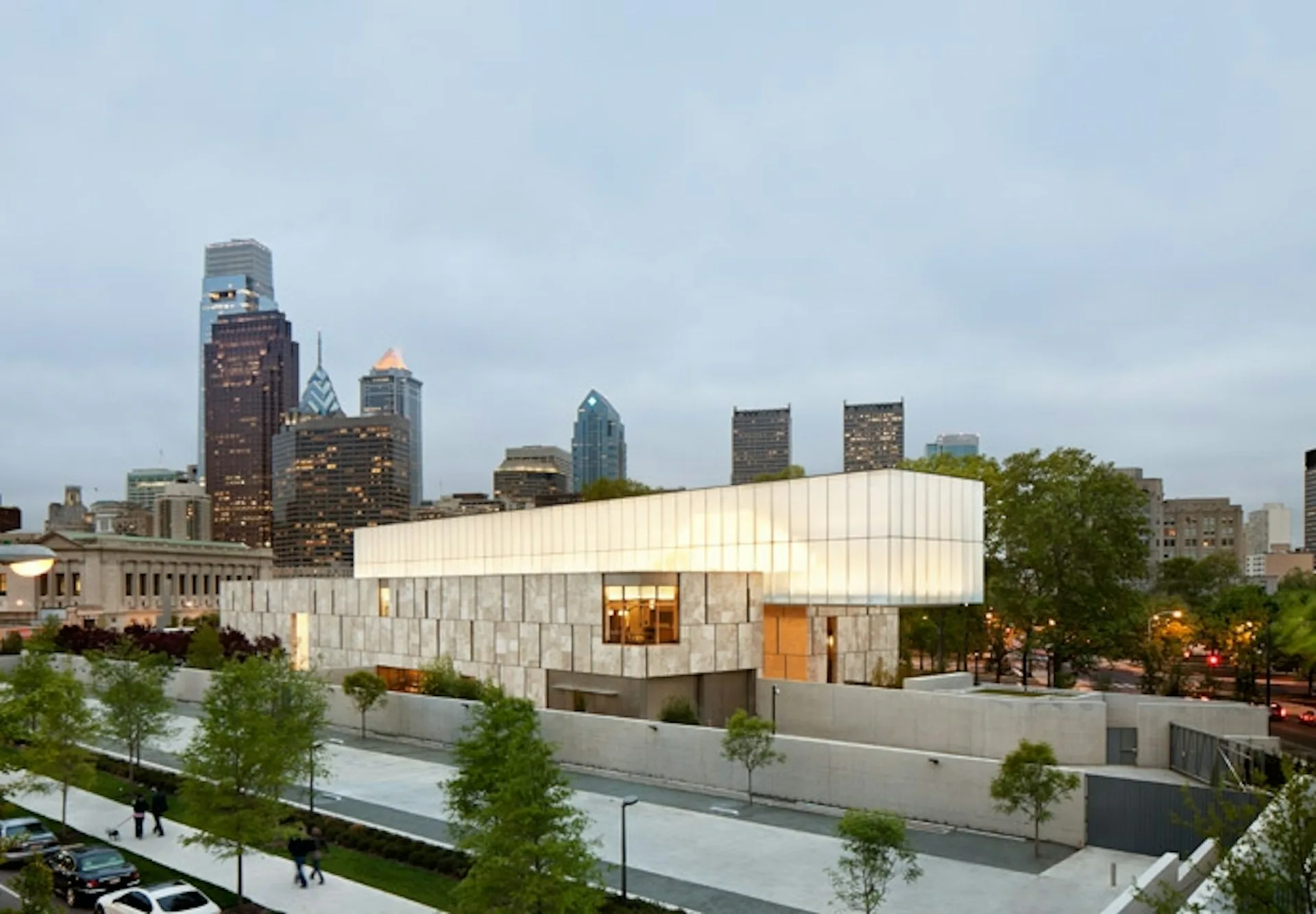 Modern white curved building with geometric facade beside waterfront and green landscaping, Dallas skyline visible behind, by Tod Williams Billie Tsien Architects | Partners.