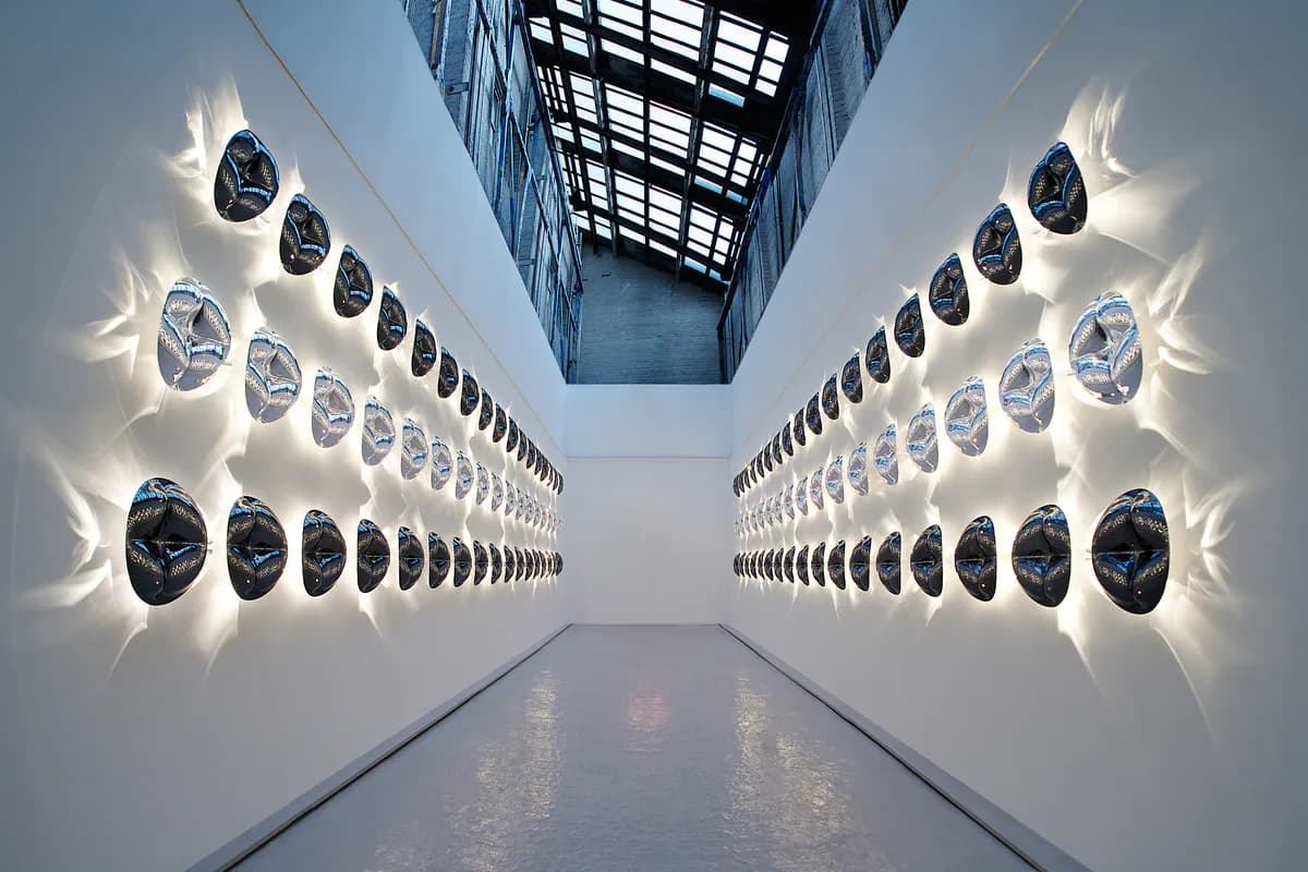 Symmetrical corridor with illuminated circular light fixtures mounted on white walls on both sides, creating a striking vanishing-point perspective by Todd Bracher Studio.