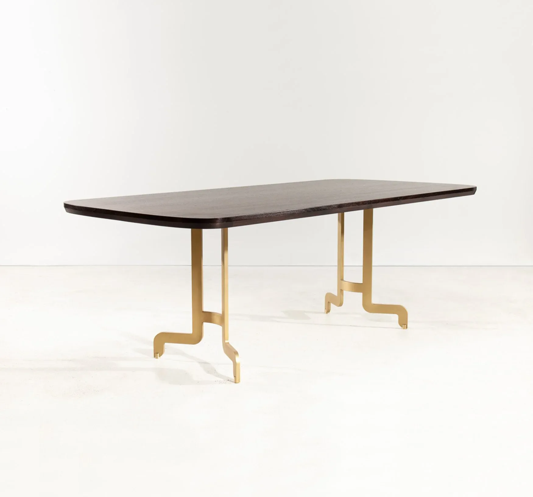 A minimalist dining table with a dark rectangular top and natural wood sculptural base featuring geometric leg supports, rendered in soft studio lighting by Token.