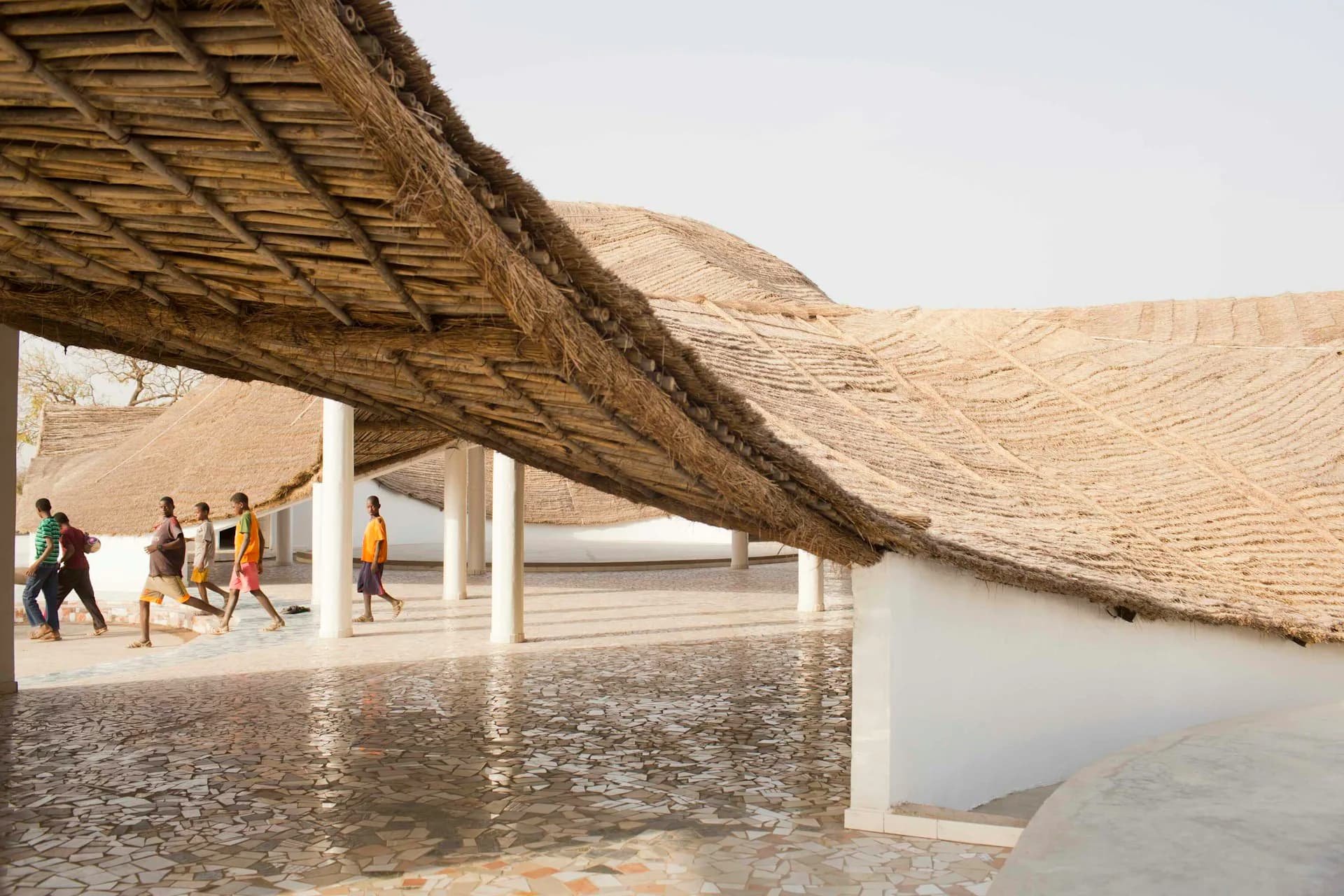 Coastal pavilion with dramatic curved wooden roof structure and open colonnade overlooking water, featuring polished concrete floors and natural materials by Toshiko Mori Architect.