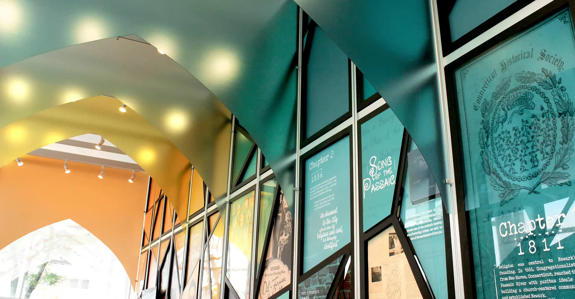 Teal gallery wall with framed exhibition displays and black metal frames, warm accent lighting overhead, by Touch Design Studio, Inc.