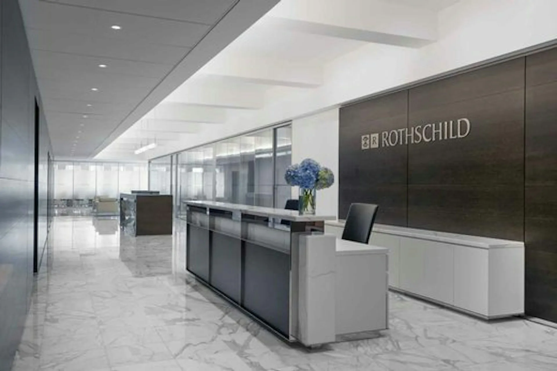 Modern office reception area with polished marble flooring, dark panel walls, white curved desk, and glass partitions, designed by TPG Architecture LLP.