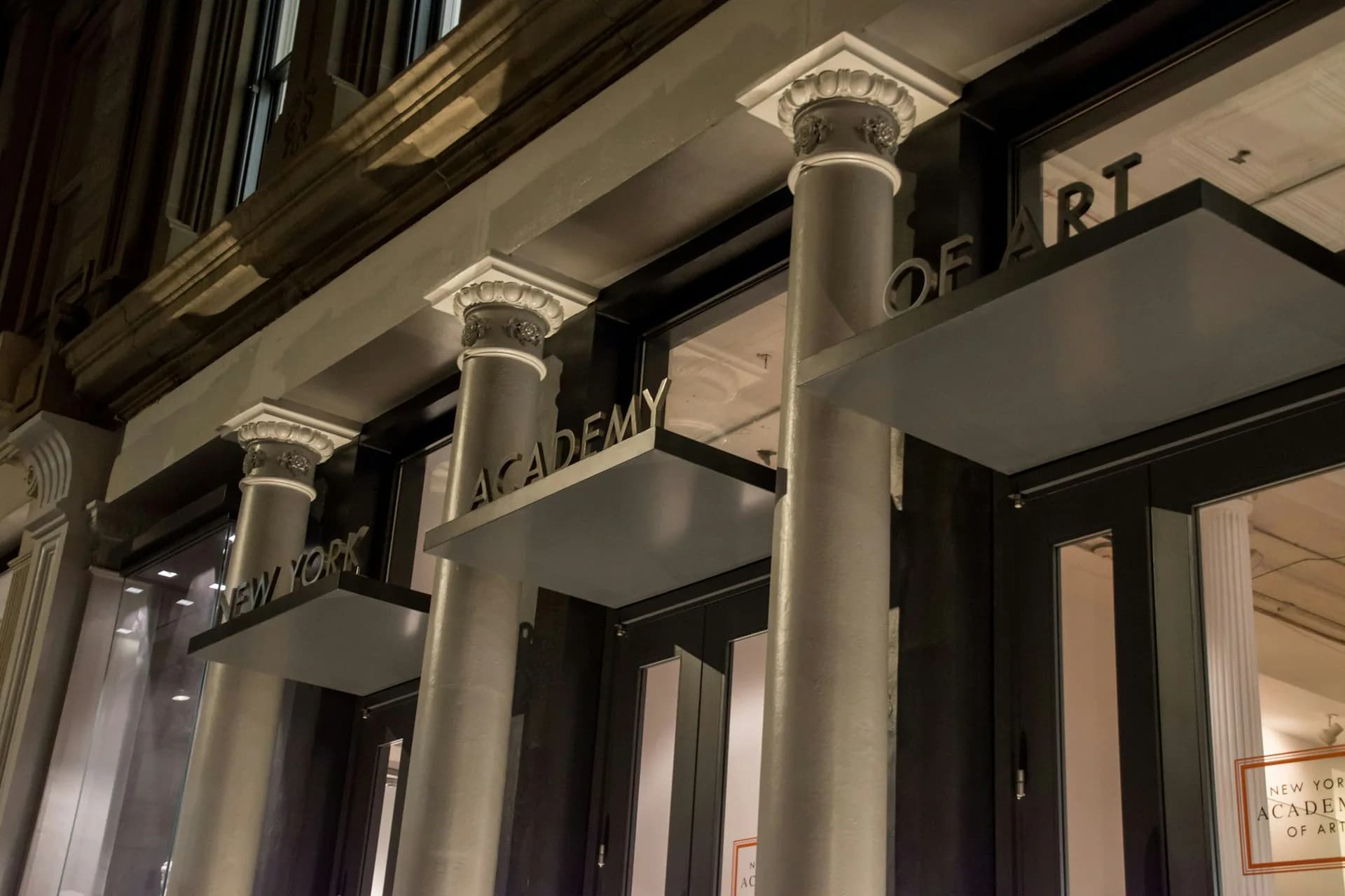 Neoclassical entrance with fluted columns and ornamental capitals, featuring dark-framed doors and signage for Academy of Art, designed by TRA studio Architecture PLLC, New York City.