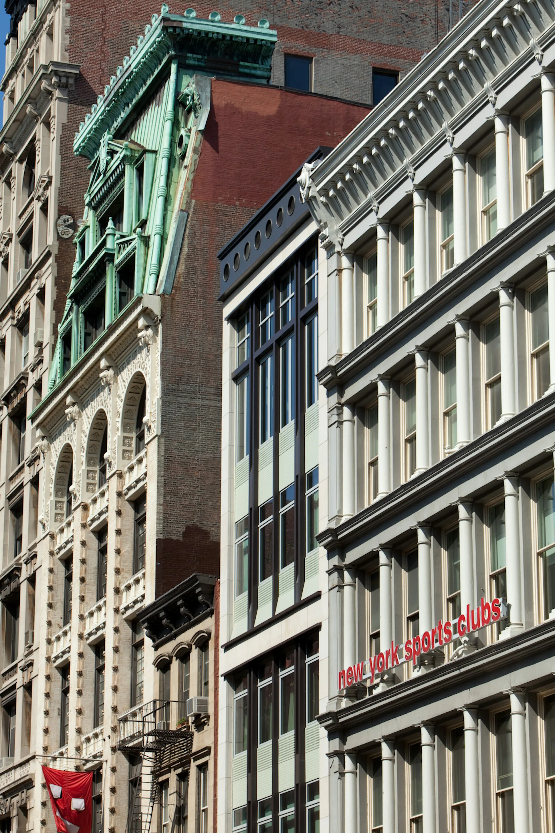 Street-level photograph of historic Manhattan buildings featuring ornate brick and stone facades with distinctive green copper architectural details and classical cornices by TRA studio Architecture PLLC, New York City.