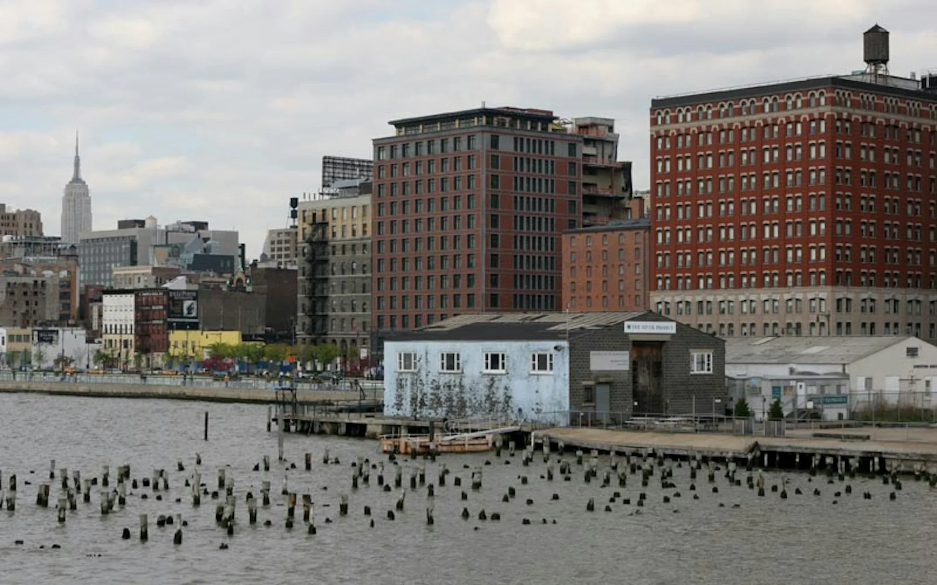 Waterfront installation with white modular structures and wooden pilings in Manhattan's East River, designed by TsAO & McKOWN Architects.
