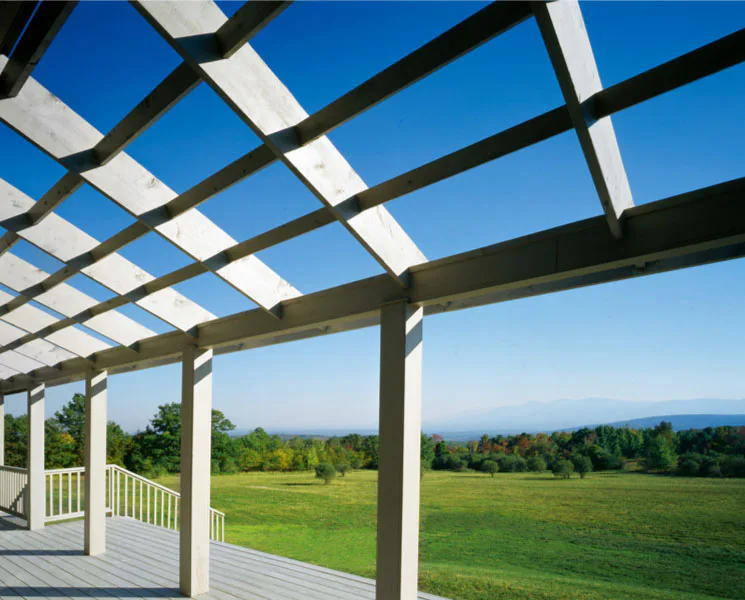 Modern pergola with white fabric panels overlooking expansive green meadows and distant mountains under clear blue sky by Turino Kalberer Architects.