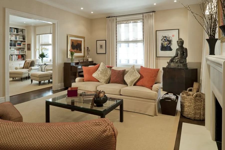 Warm-toned living room featuring a cream sofa with coral and gold pillows, dark wood furniture, framed artwork, and views to adjacent spaces, designed by Turino Kalberer Architects.