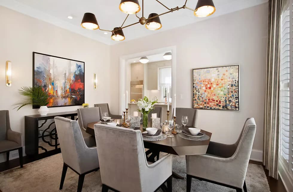 Modern dining room with gray upholstered chairs, dark table, brass chandelier, and colorful abstract artwork on cream walls by Twelfth Street Interiors.