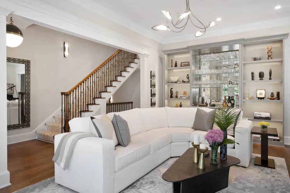 Contemporary living room with curved cream sofa, built-in shelving, wooden staircase, and polished hardwood floors designed by Twelfth Street Interiors.