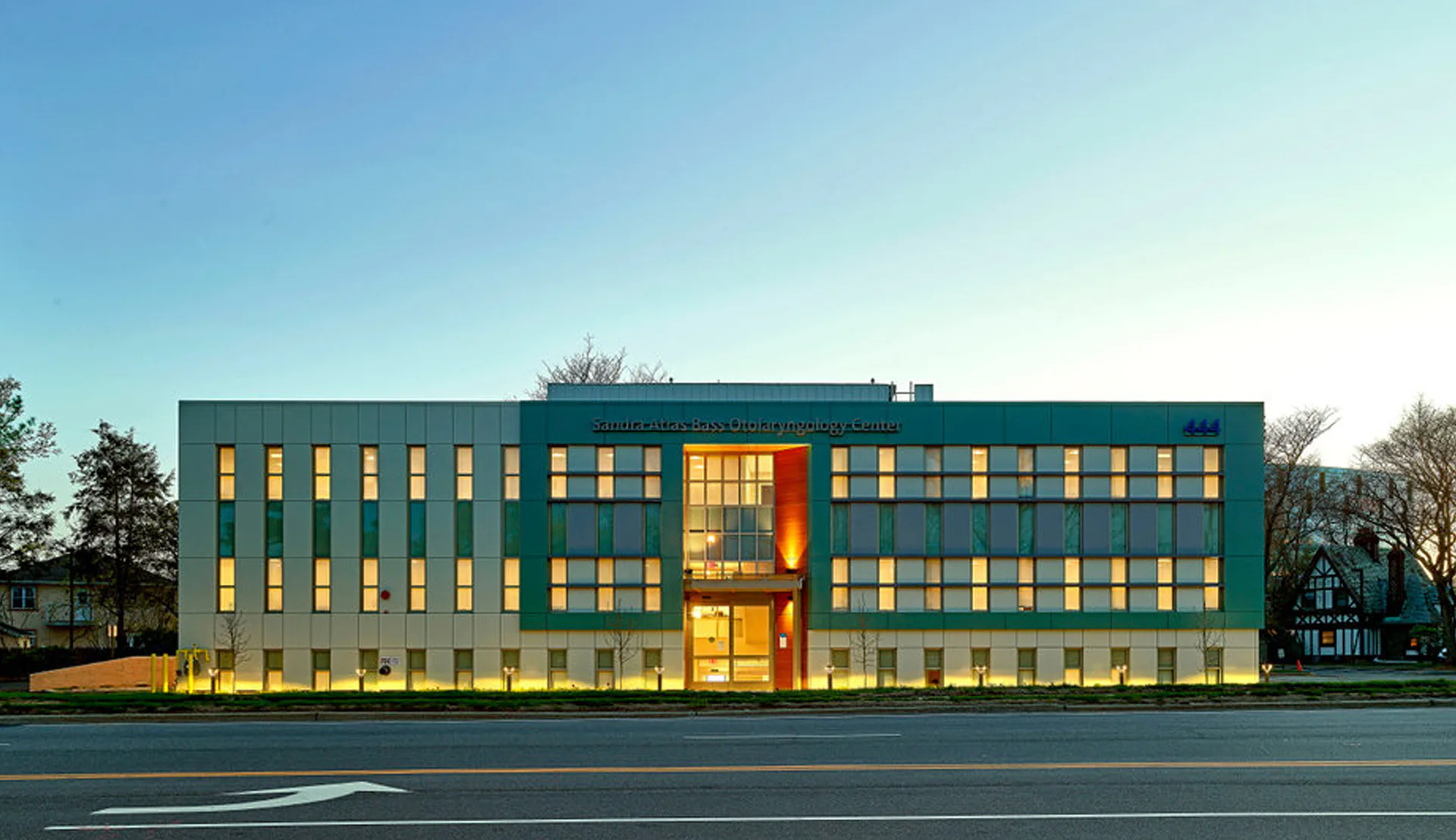 Modern institutional building with teal and yellow facades, illuminated at dusk, featuring rhythmic window patterns and a central golden entrance element by Twine Architectural Studio.