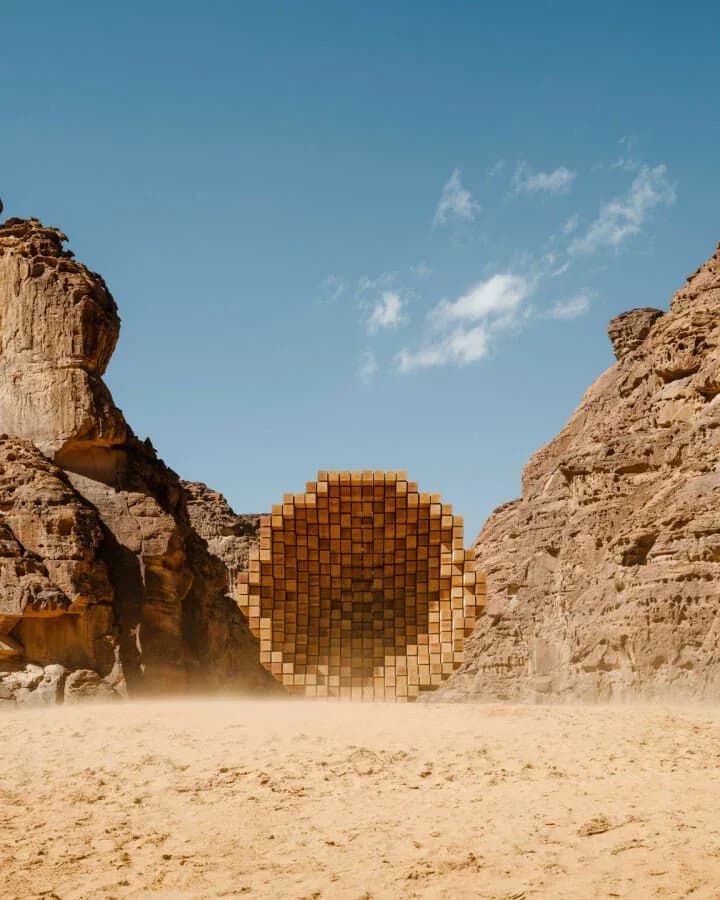 Desert landscape with natural rock formations flanking a geometric pixelated golden sphere installation in sand by UAP (Urban Art Projects).