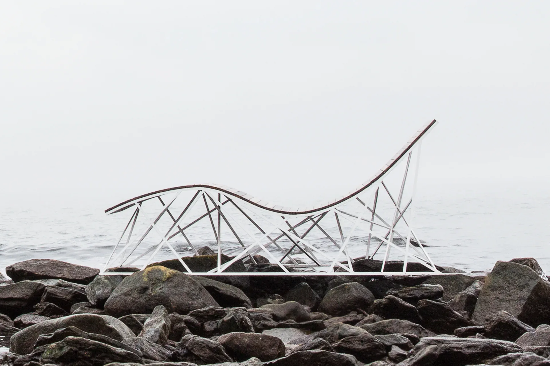 Sculptural metal installation on rocky shoreline with geometric wire framework structure overlooking misty water, by Uhuru Design.