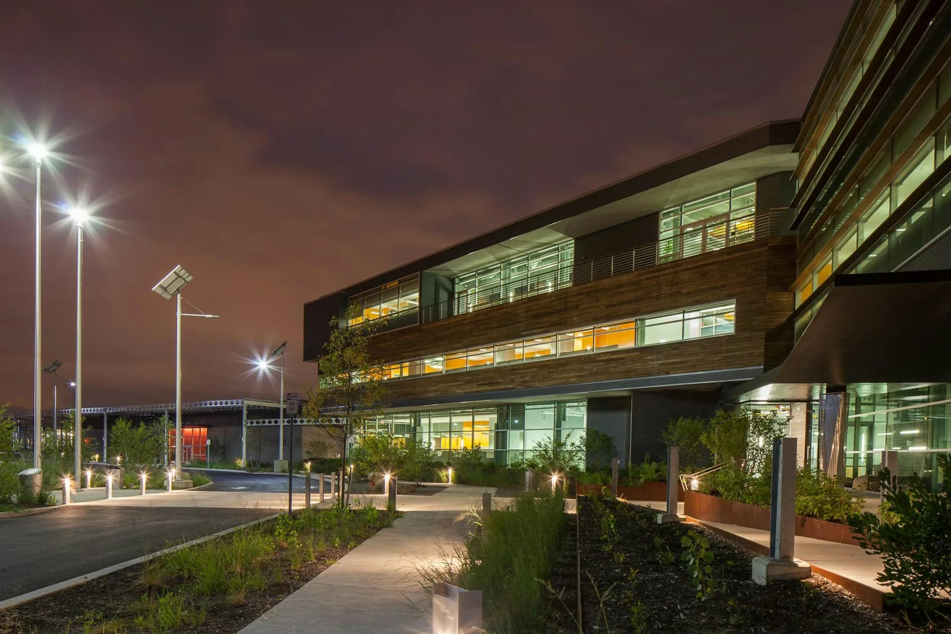 Modern brick institutional building photographed at dusk with illuminated windows, clean landscaping, and contemporary lighting design by Urbahn Architects.