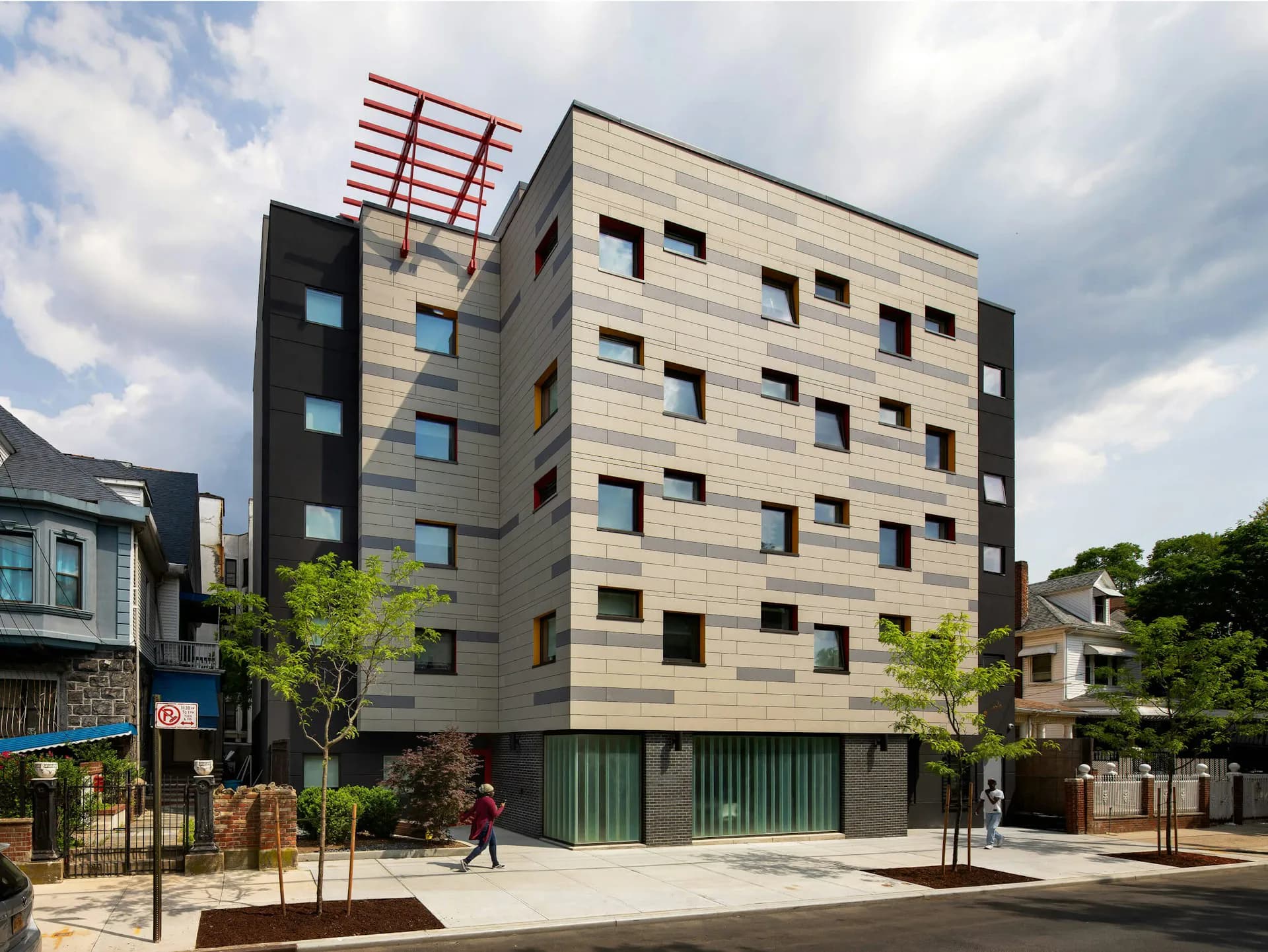 Modern mixed-use residential building with cream-colored stone facade, dark vertical striping, and green ground-floor storefront, designed by Urban Architectural Initiatives.