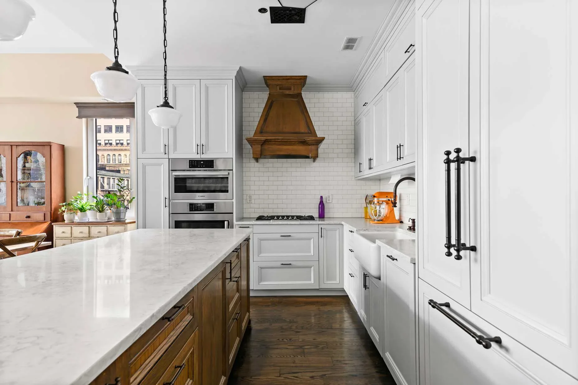 Modern kitchen with white cabinetry, marble countertops, wood island, bronze range hood, and pendant lighting by Urban Homecraft.