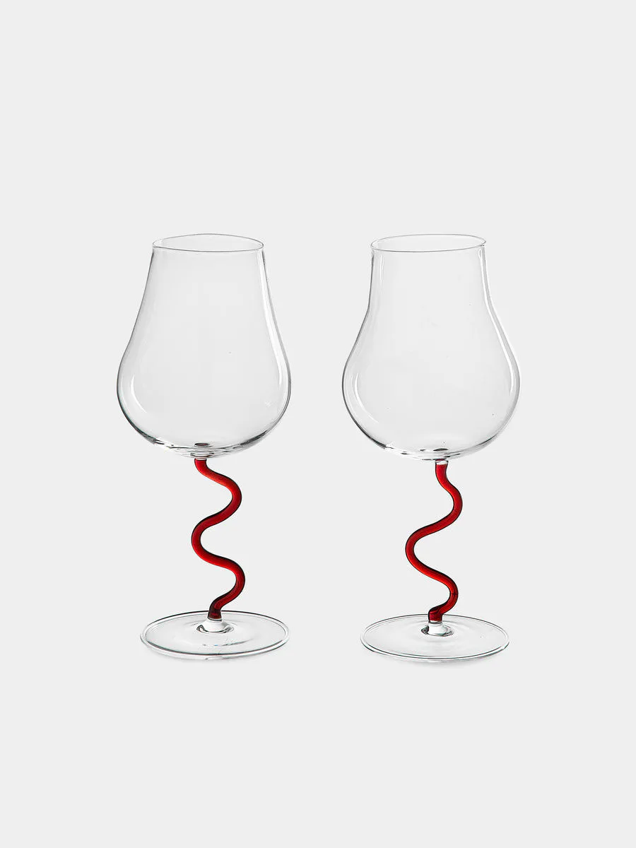 Two elegant wine glasses with sinuous red curved stems against a neutral background by UrbanGlass.