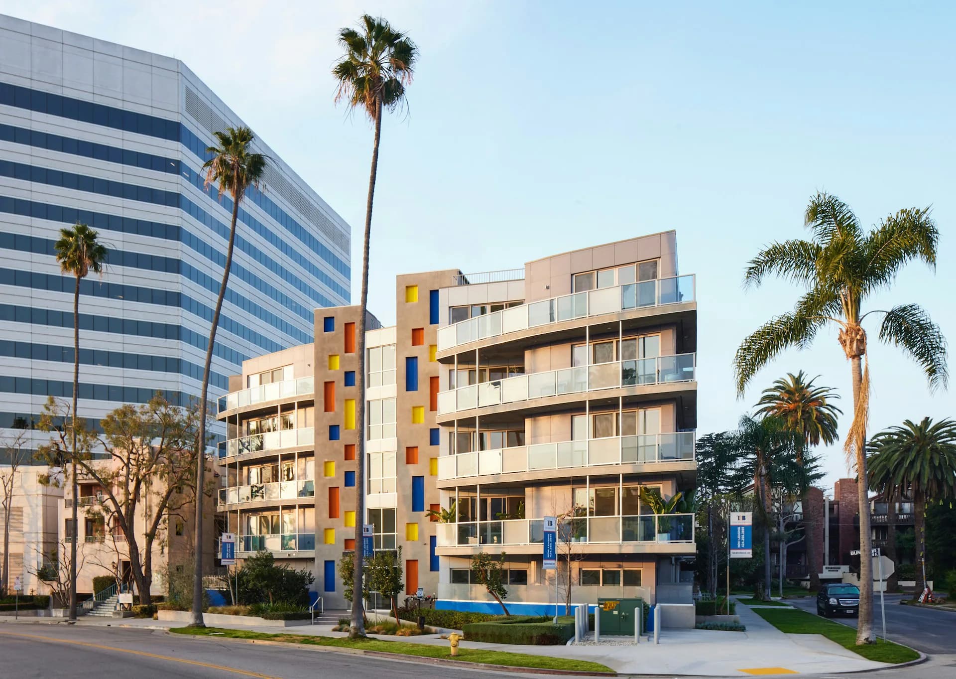 Colorful mid-rise residential building with yellow and blue facade, balconies, and palm trees in urban setting by Valerie Schweitzer Architects (VSA).