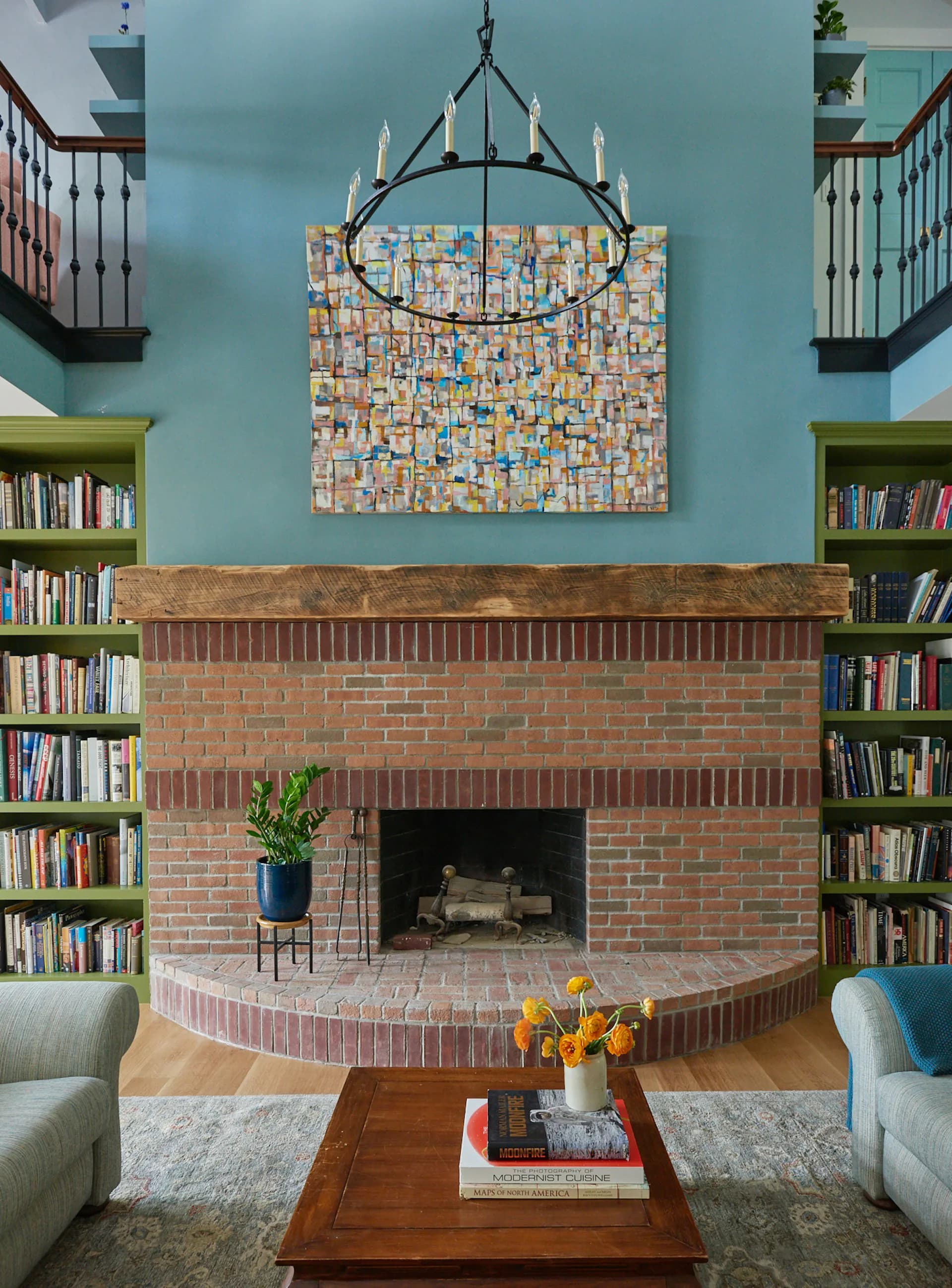 A bright turquoise living room with a brick fireplace flanked by built-in bookshelves, featuring a modern chandelier and contemporary furnishings by Valerie Schweitzer Architects (VSA).
