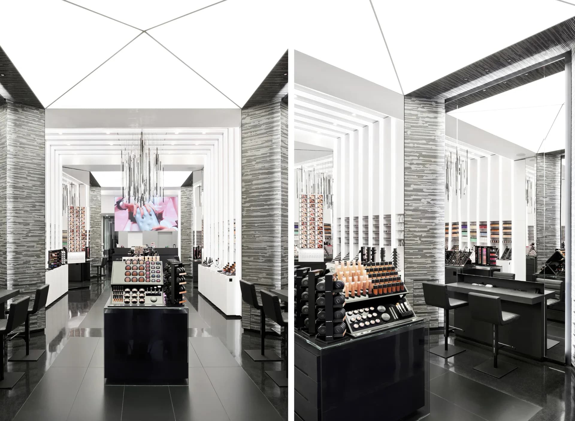 Luxury cosmetics retail space with symmetrical layout, white geometric ceiling details, exposed brick walls, and black display tables with product arrangements, by Ventresca Lighting Designers.