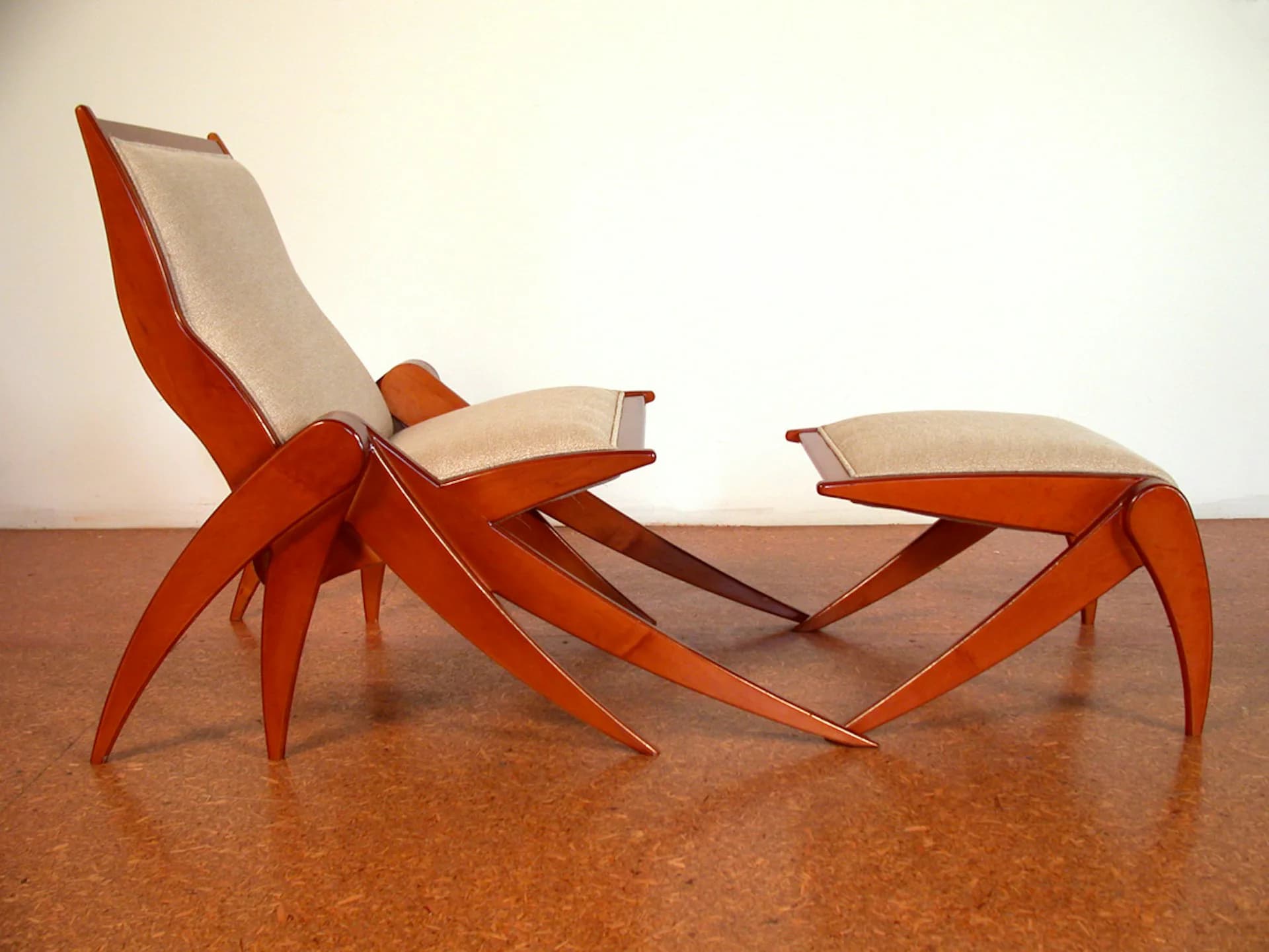 Red and cream sculptural furniture pieces with geometric spider-like legs and fabric slings on a cork surface, designed by VIRALINE Architecture LLP.
