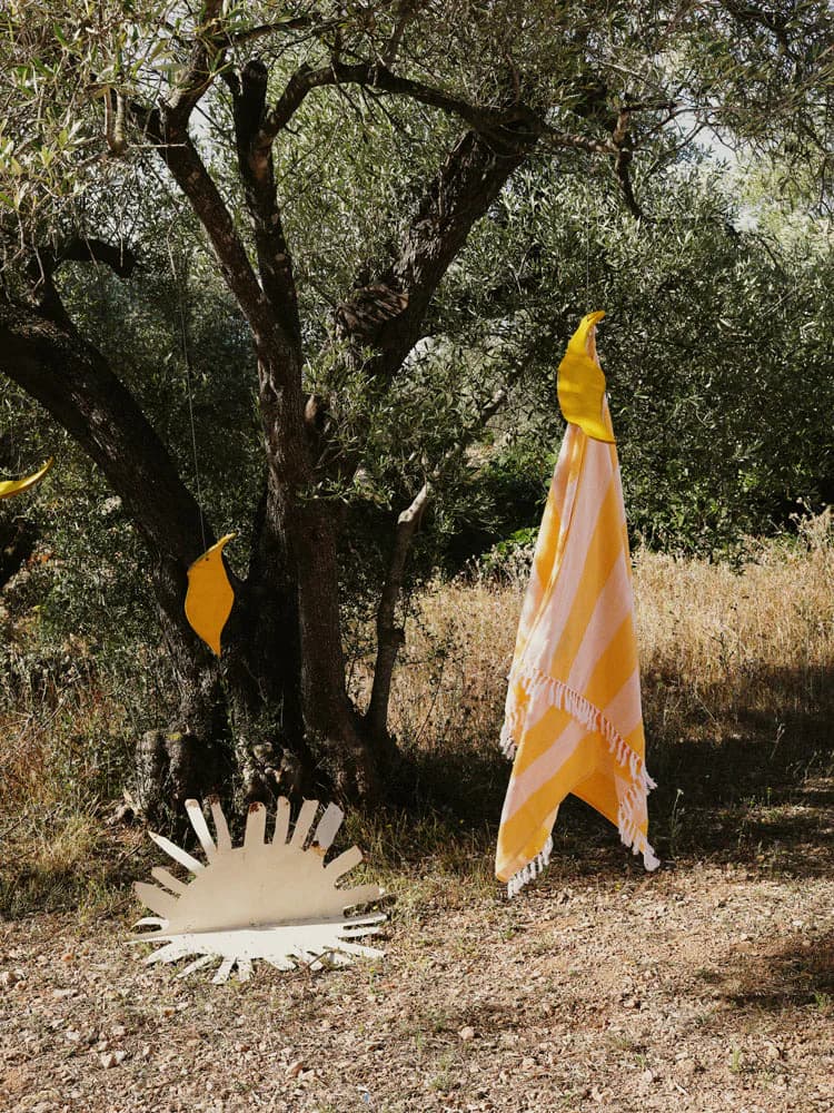 Olive grove landscape installation featuring a sculptural white sun form and yellow draped textile elements by Viso Project.
