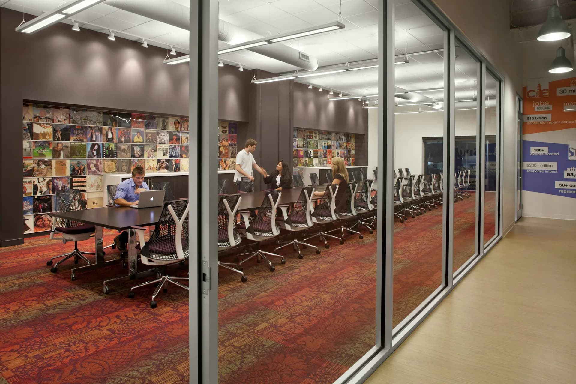 Modern office workspace with glass partitions, red patterned carpet, ergonomic seating, and collaborative desk areas with inspiration boards, designed by Vocon.