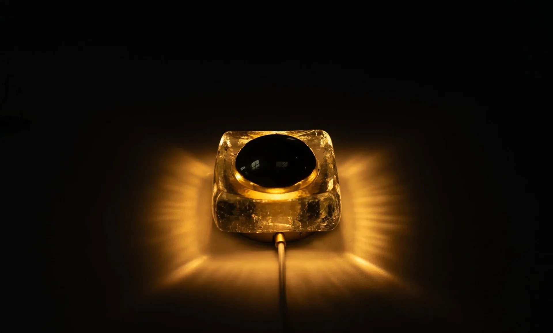 Golden textured sculptural lighting fixture with black spherical center emitting warm ambient light, by Voidfill Studio.
