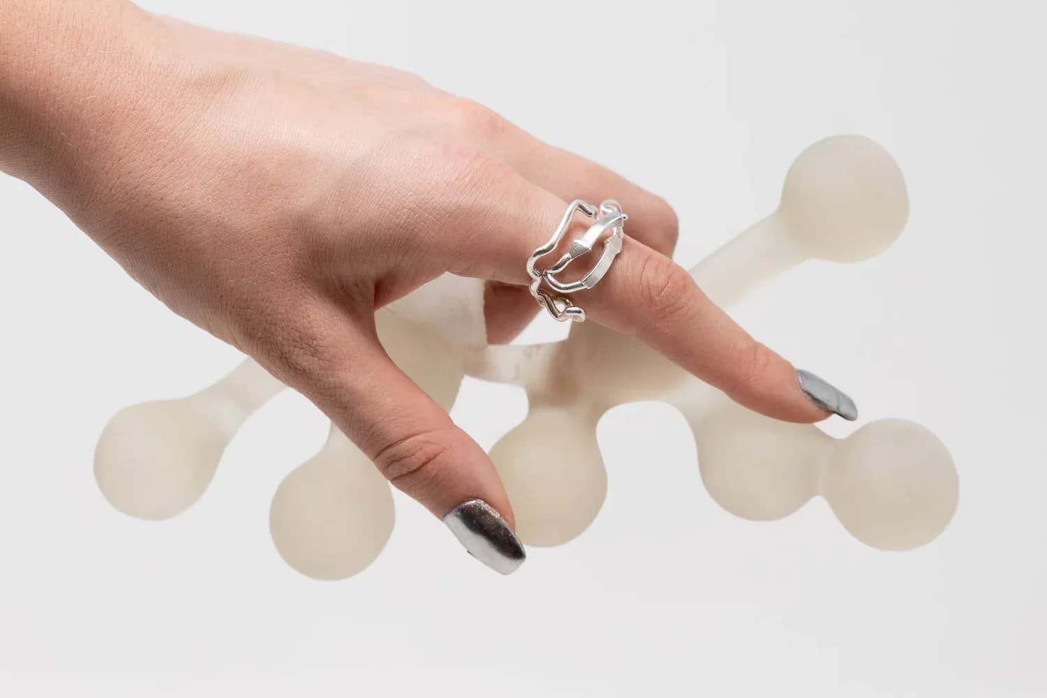 Hand wearing silver chunky link ring and dark nail polish, photographed against white background with frosted glass spheres, by Voidfill Studio.