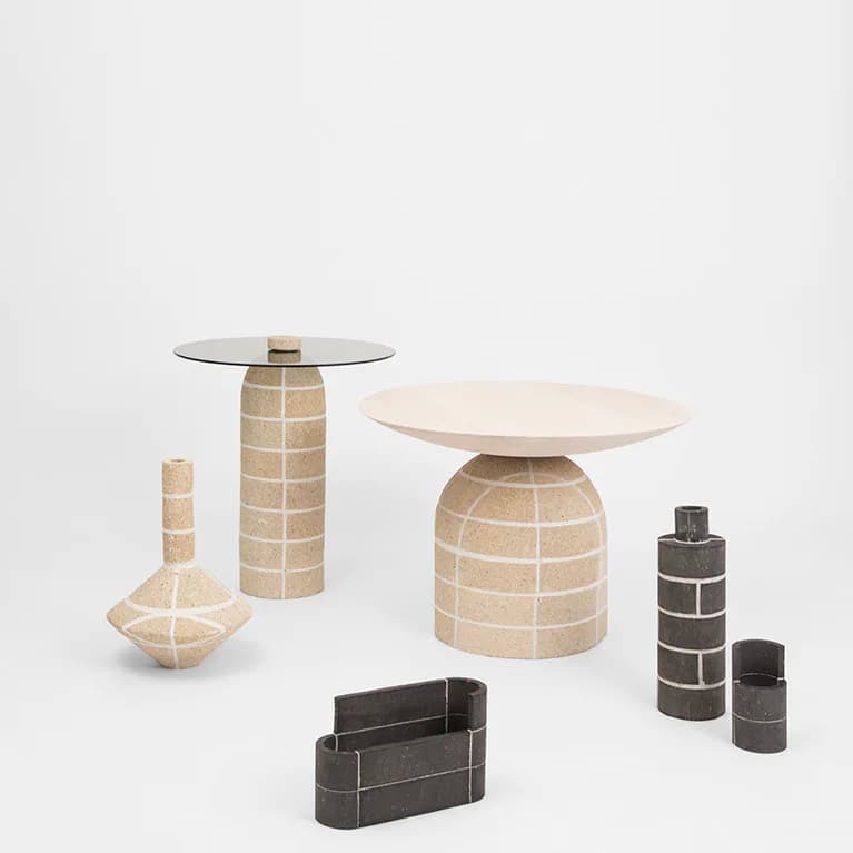 Collection of sculptural furniture pieces featuring geometric forms in natural wood and dark materials with grid patterns, displayed against a neutral background by Vonnegut/Kraft.