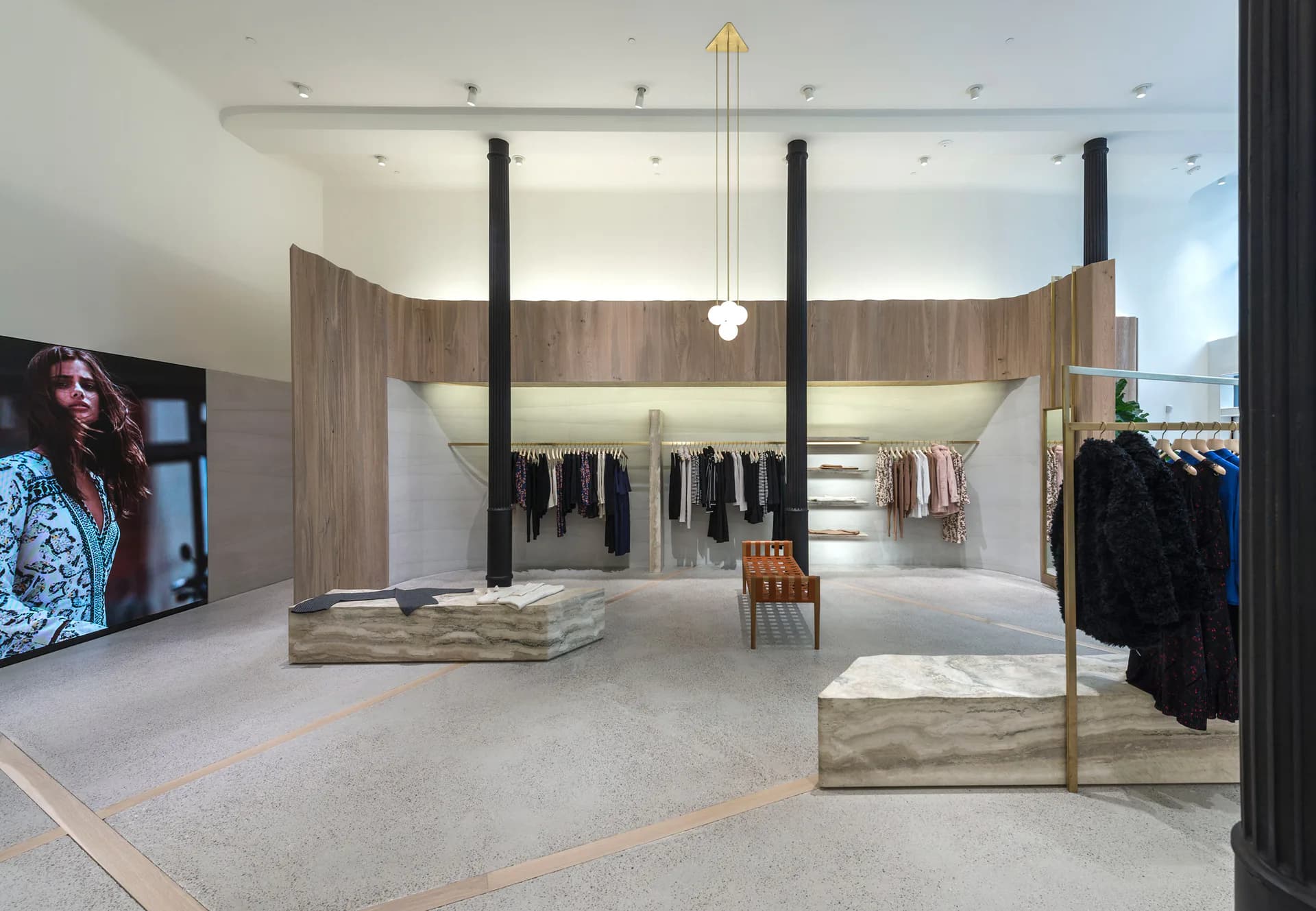 Modern retail clothing showroom with curved timber partitions, glass display cases, pendant lighting, and mirrored walls creating an open, gallery-like shopping environment by Vonnegut/Kraft.