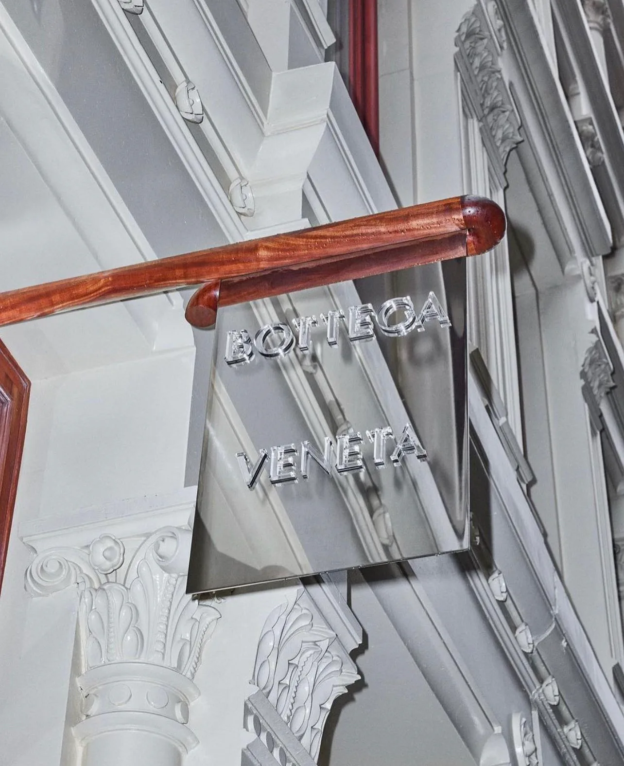 Elegant staircase detail featuring a polished wooden handrail and ornamental white plaster capital, with signage reading 'BOTTEGA VENETA' mounted on the wall by Vonnegut/Kraft.