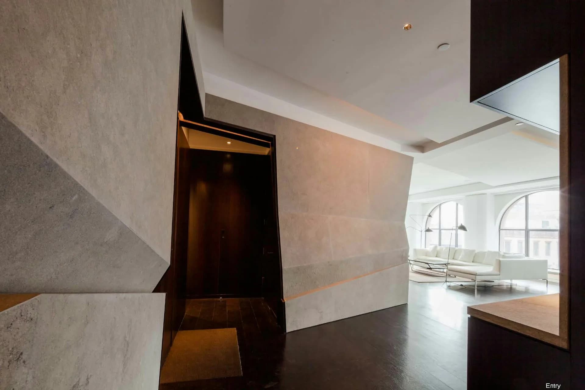 Modern interior hallway with dark wood pivot door, white ceiling details, and view into bright gallery space with arched windows, designed by Voorsanger Architects PC.