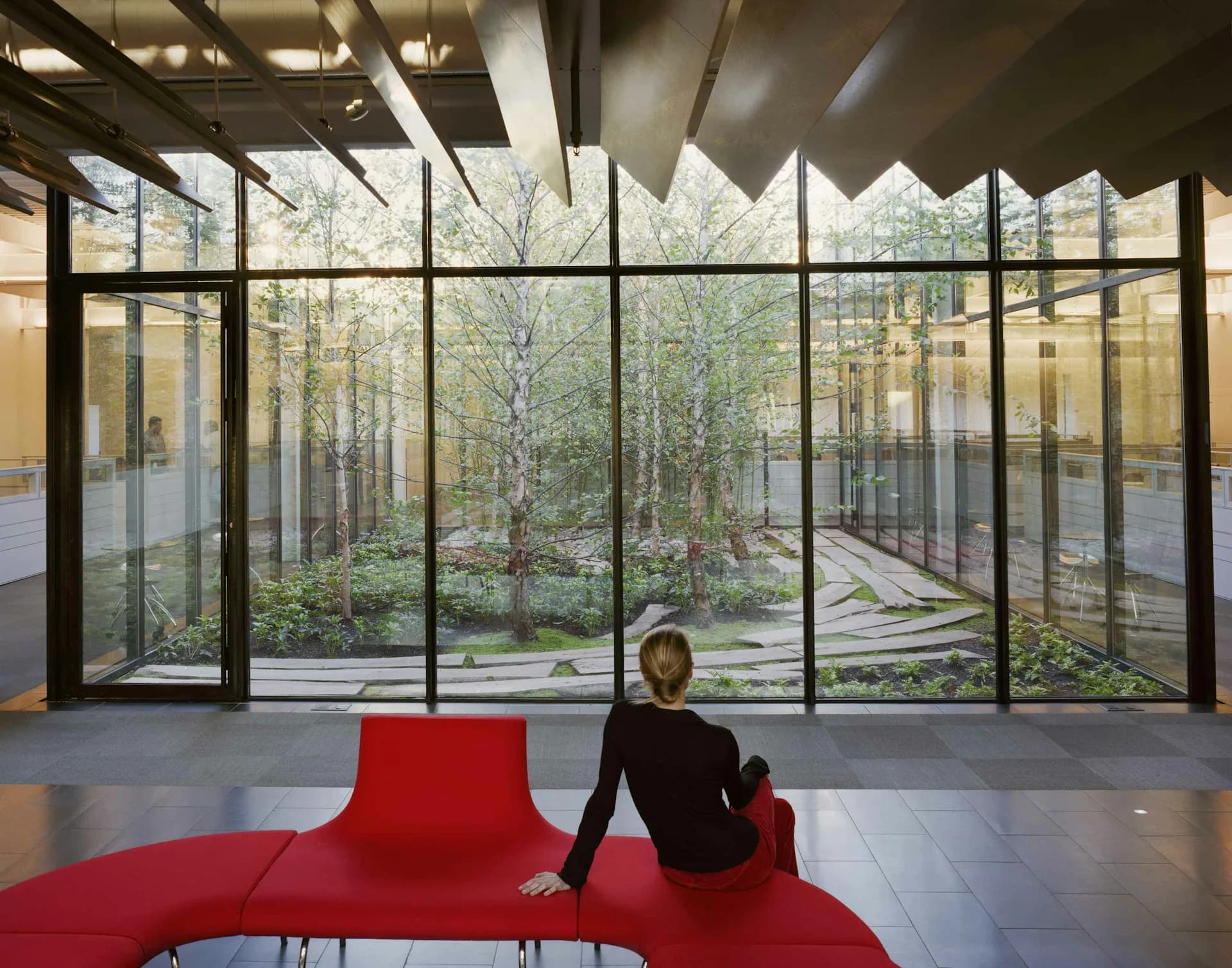 Modern interior with expansive gridded glass walls overlooking a forest courtyard, featuring a sculptural red seating element, designed by Voorsanger Architects PC.