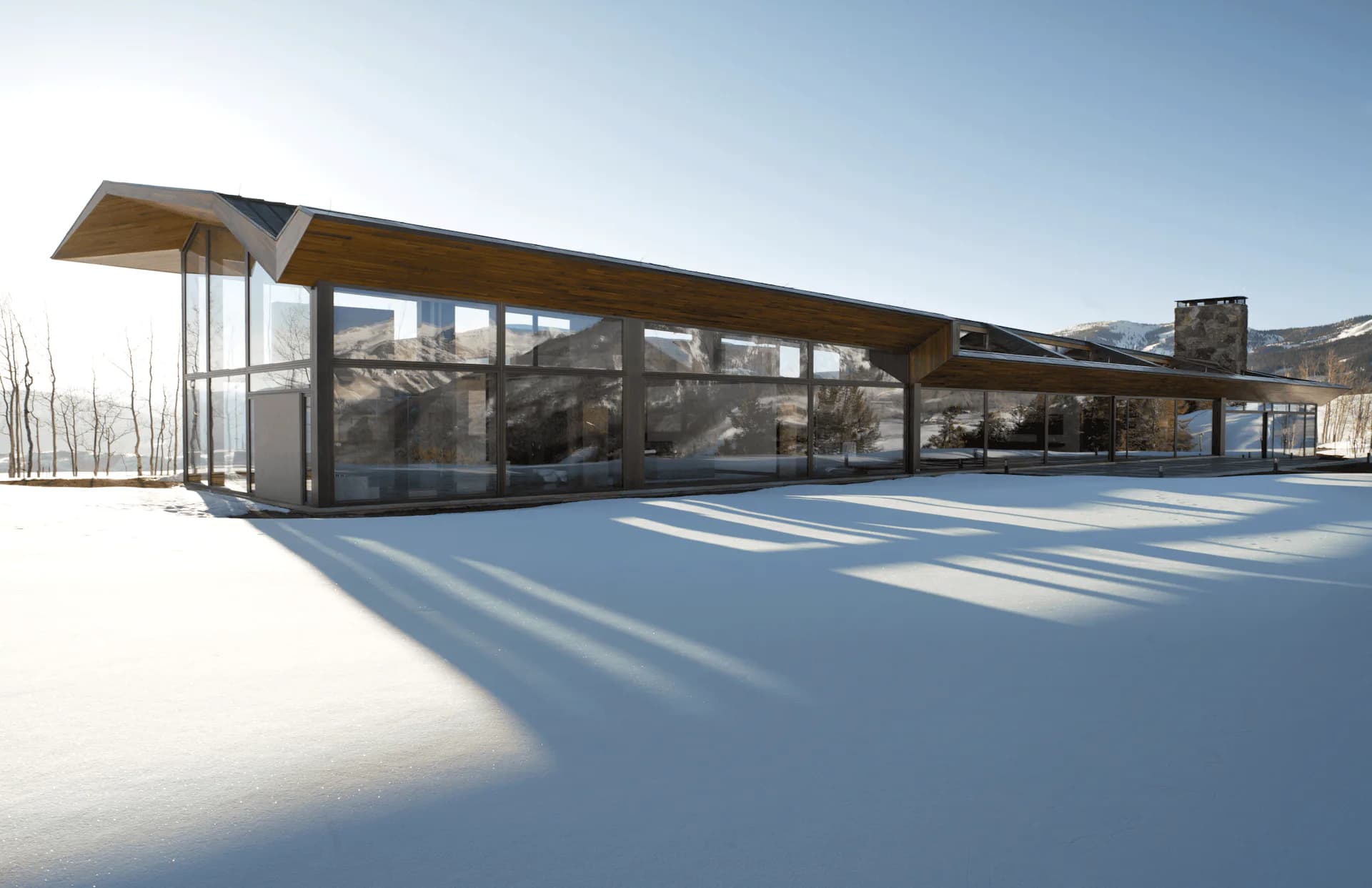 Modern glass and wood pavilion with extended cantilever roof casting geometric shadows across snow-covered ground, designed by Voorsanger Architects PC.