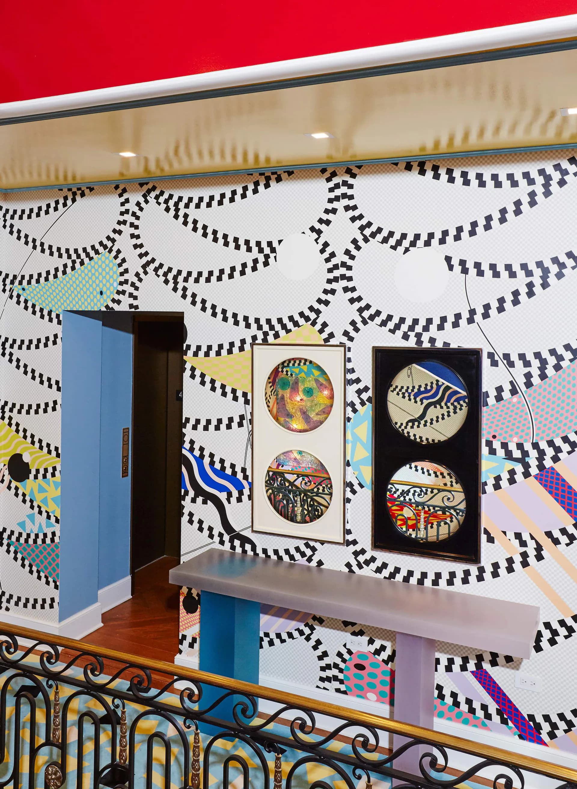 Modern interior with bold black and white patterned wallpaper, red ceiling, blue doorway, and display wall featuring colorful circular artworks by Voutsa.