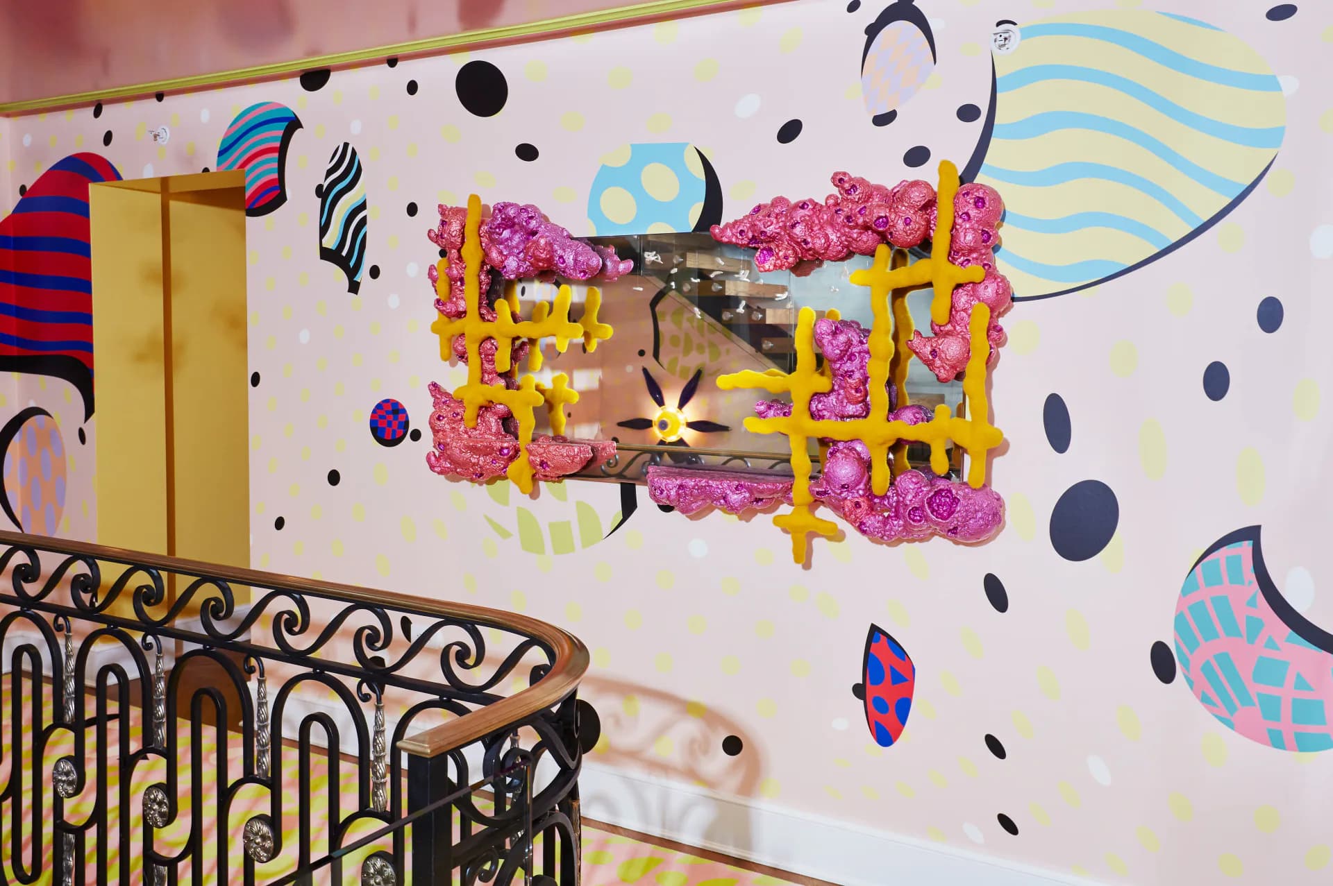 Vibrant ceiling installation featuring pink floral elements, yellow geometric frames, and colorful abstract wall graphics with playful patterns by Voutsa.