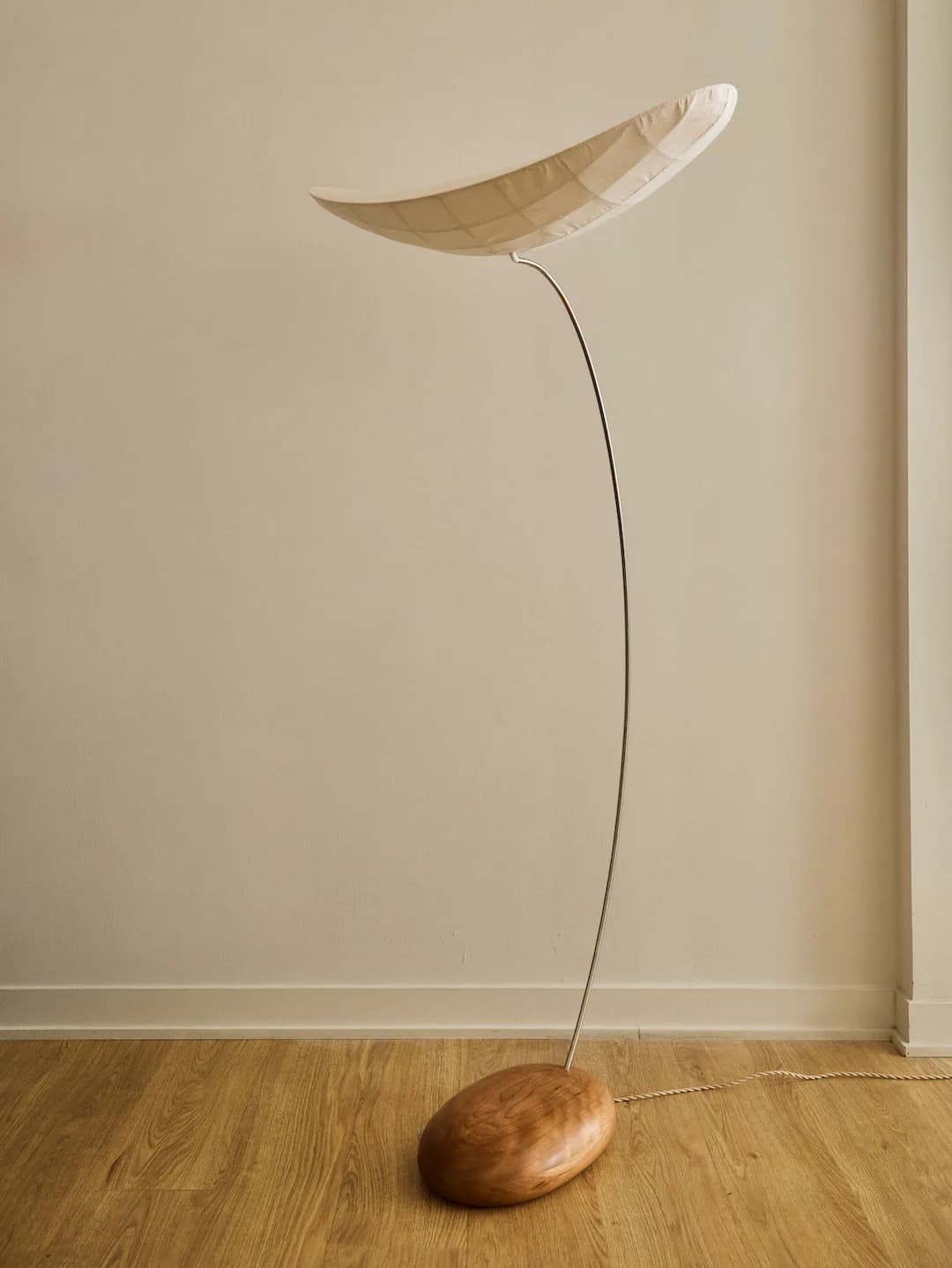 Minimalist sculptural installation with curved wooden element suspended above wooden base by thin wire against neutral wall by Vy Voi.