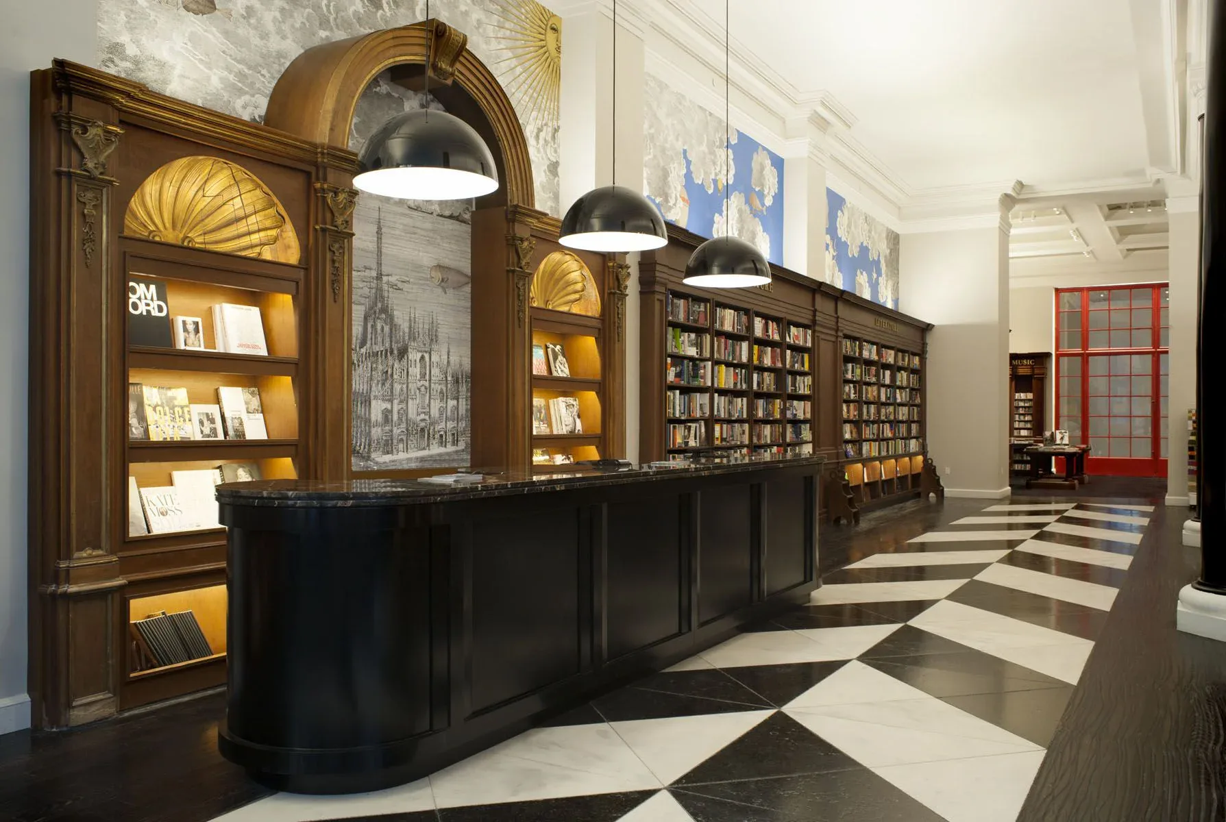 Luxury library interior with dark wood cabinetry, brass-accented arched shelving, black pendant lights, and geometric black-and-white flooring by WALD Studio.